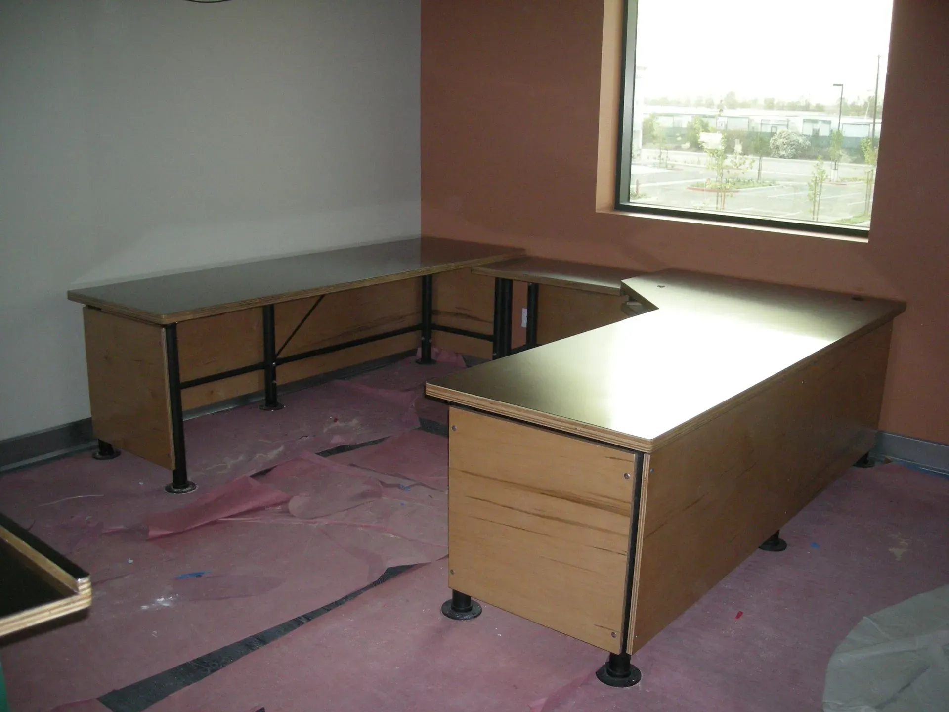 Empty office with two wooden desks on a pink carpet near a window.