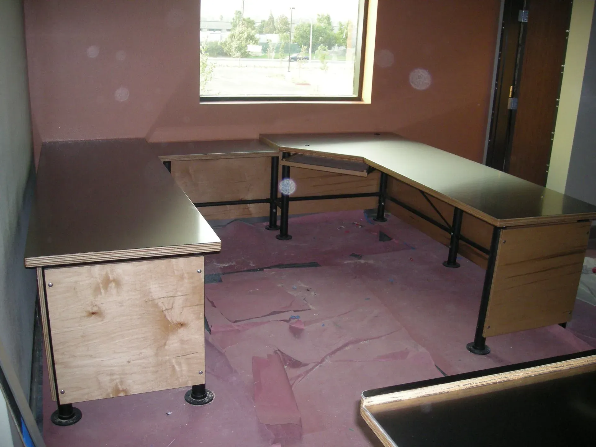 U-shaped office desk setup in an empty room with pink walls and a window.