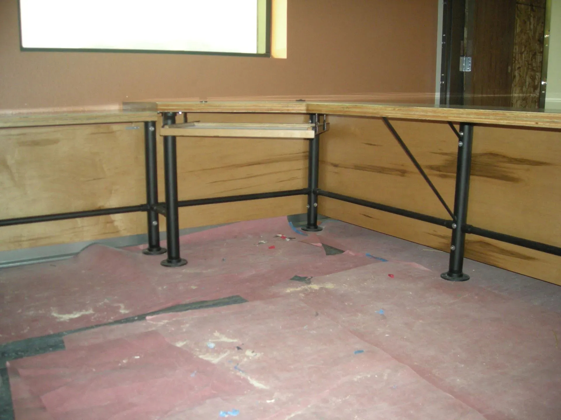 Empty indoor room with a long wooden table frame on metal legs against tan walls