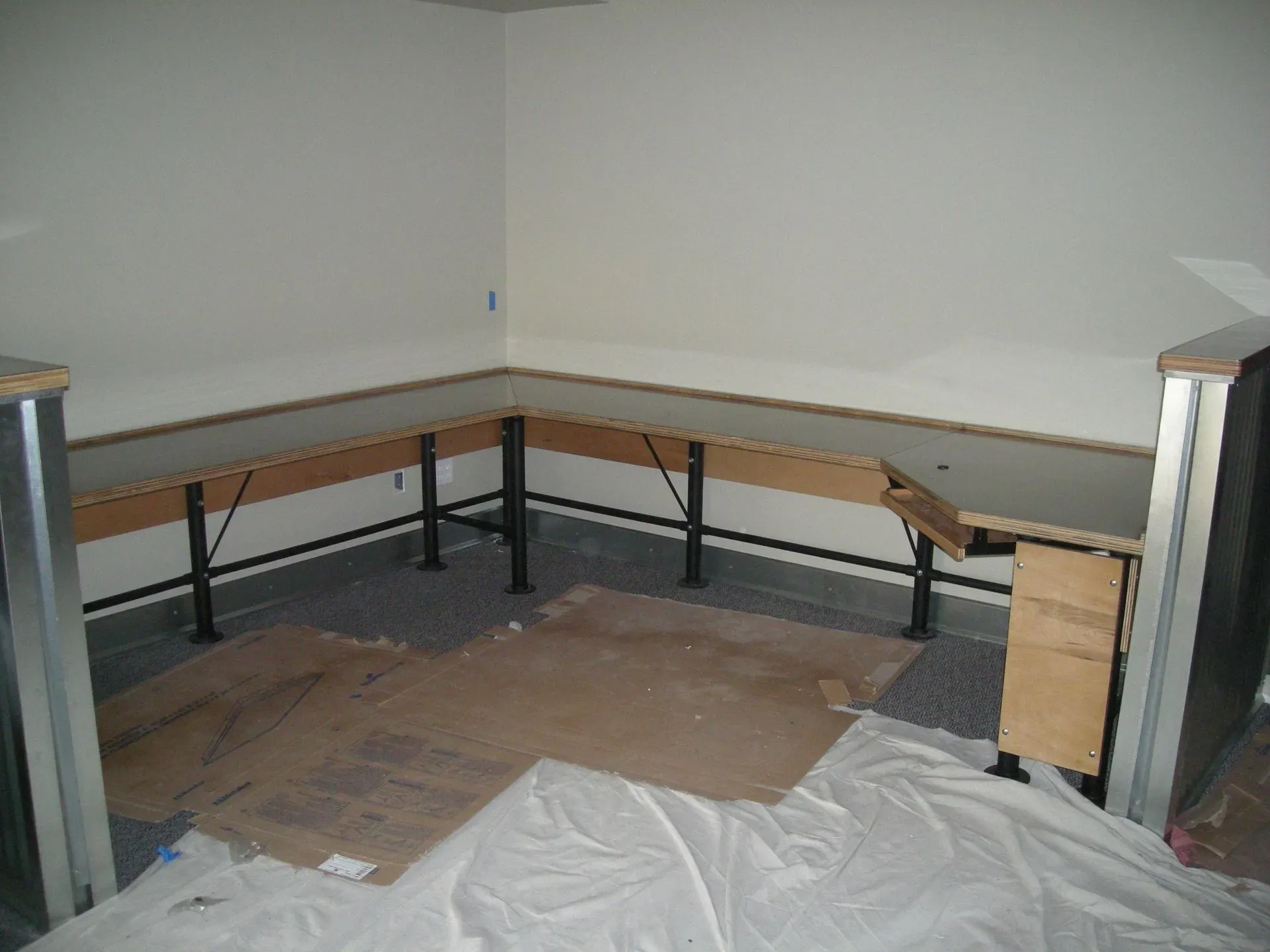 Empty room with L-shaped workbench, bare walls, and cardboard-covered floor under construction