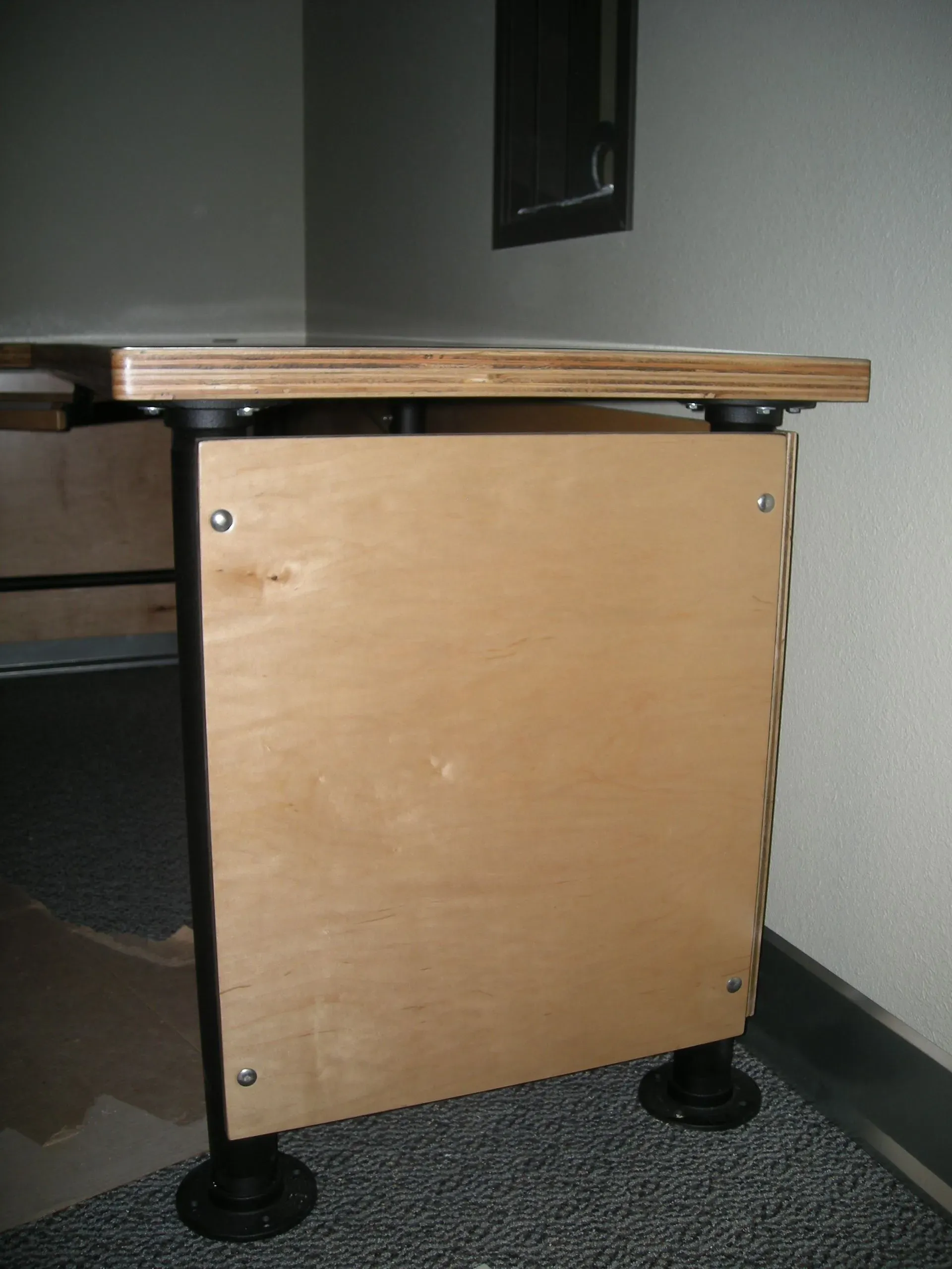 Small wooden desk with a light wood side panel and black legs on a carpeted floor.