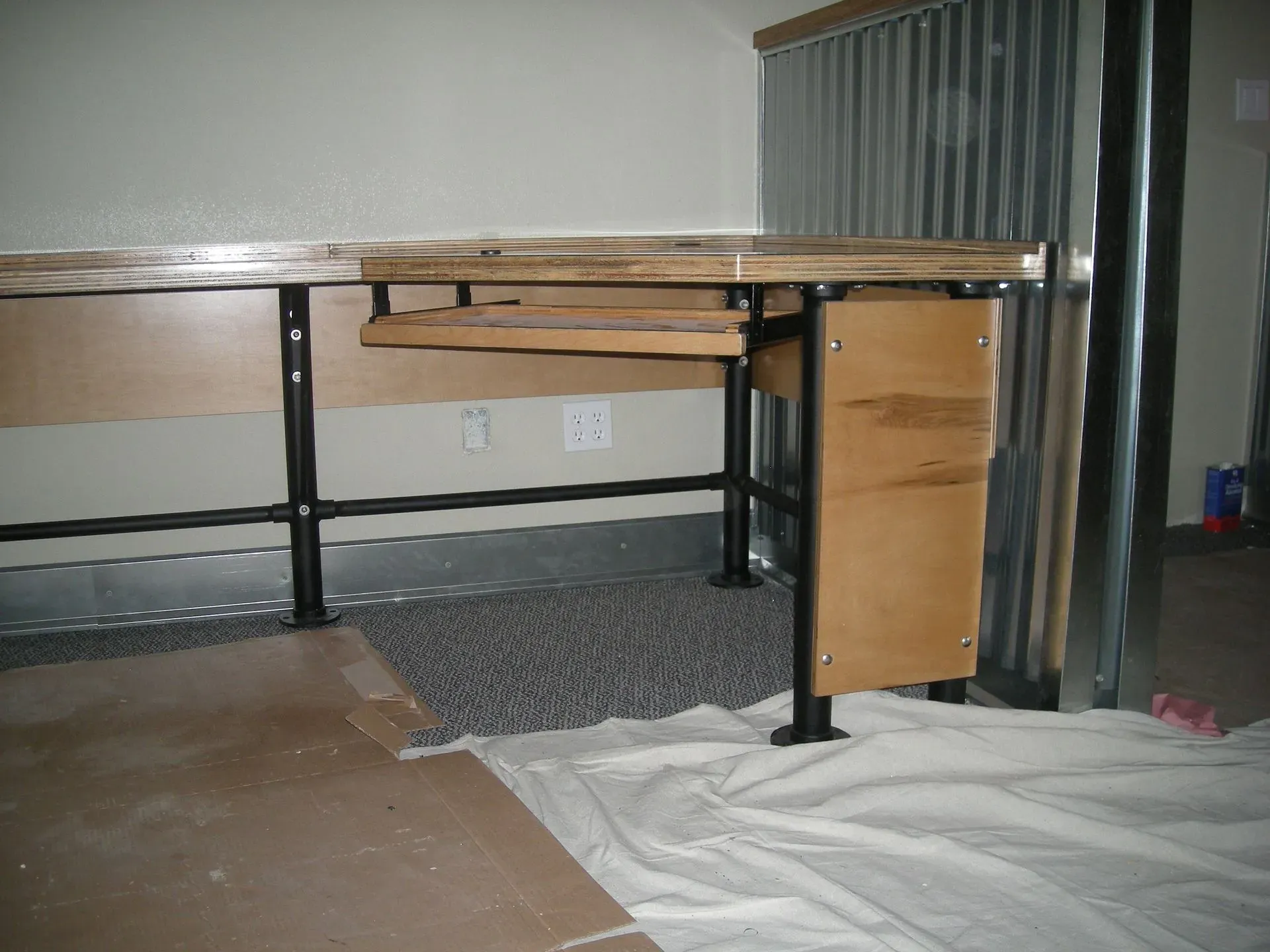 Office desk with drawers and black legs, partially covered by a white tarp, in an unfinished room