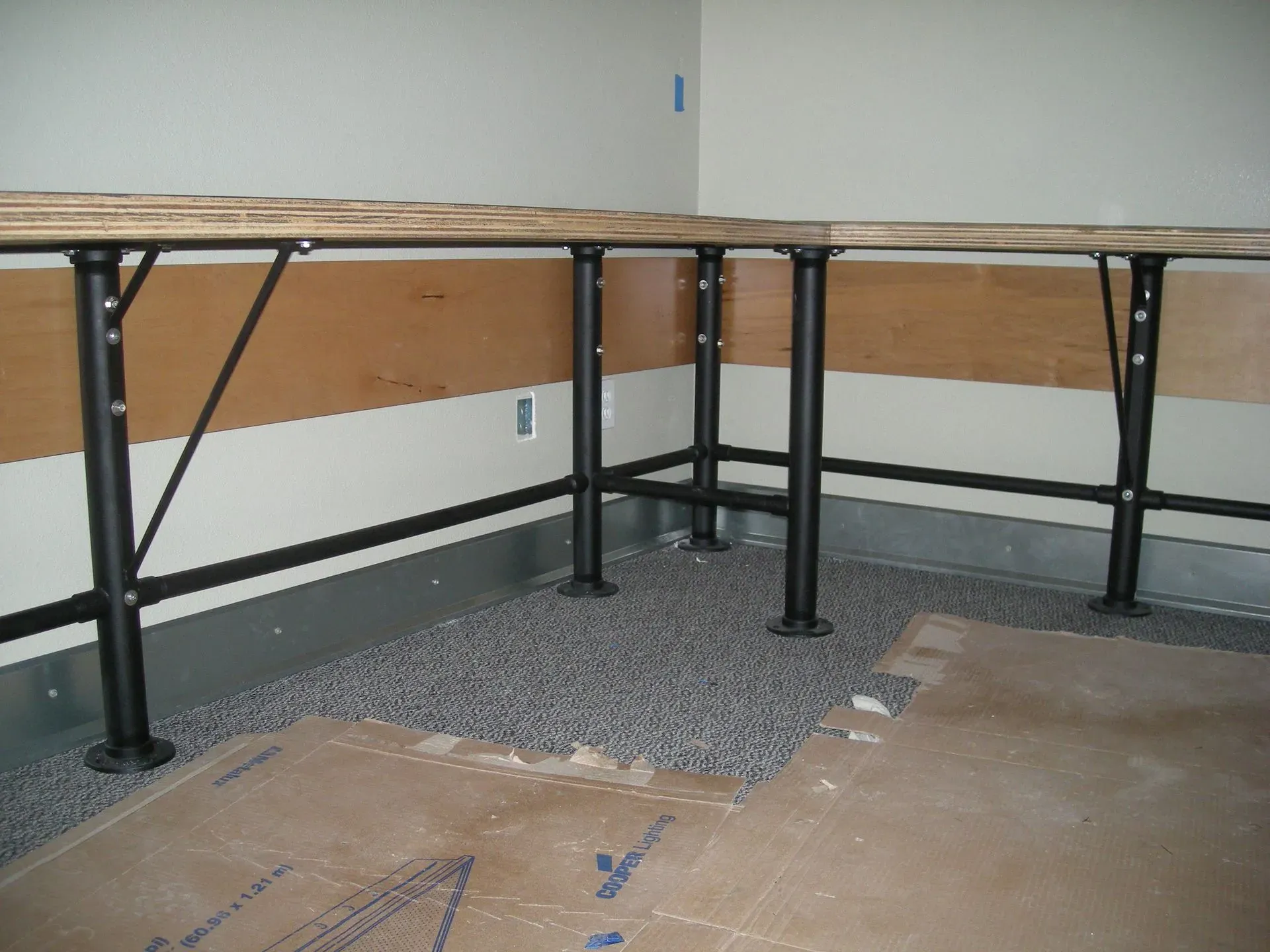 Foldable tables lined against walls in a sparse room with carpet and bare floor.