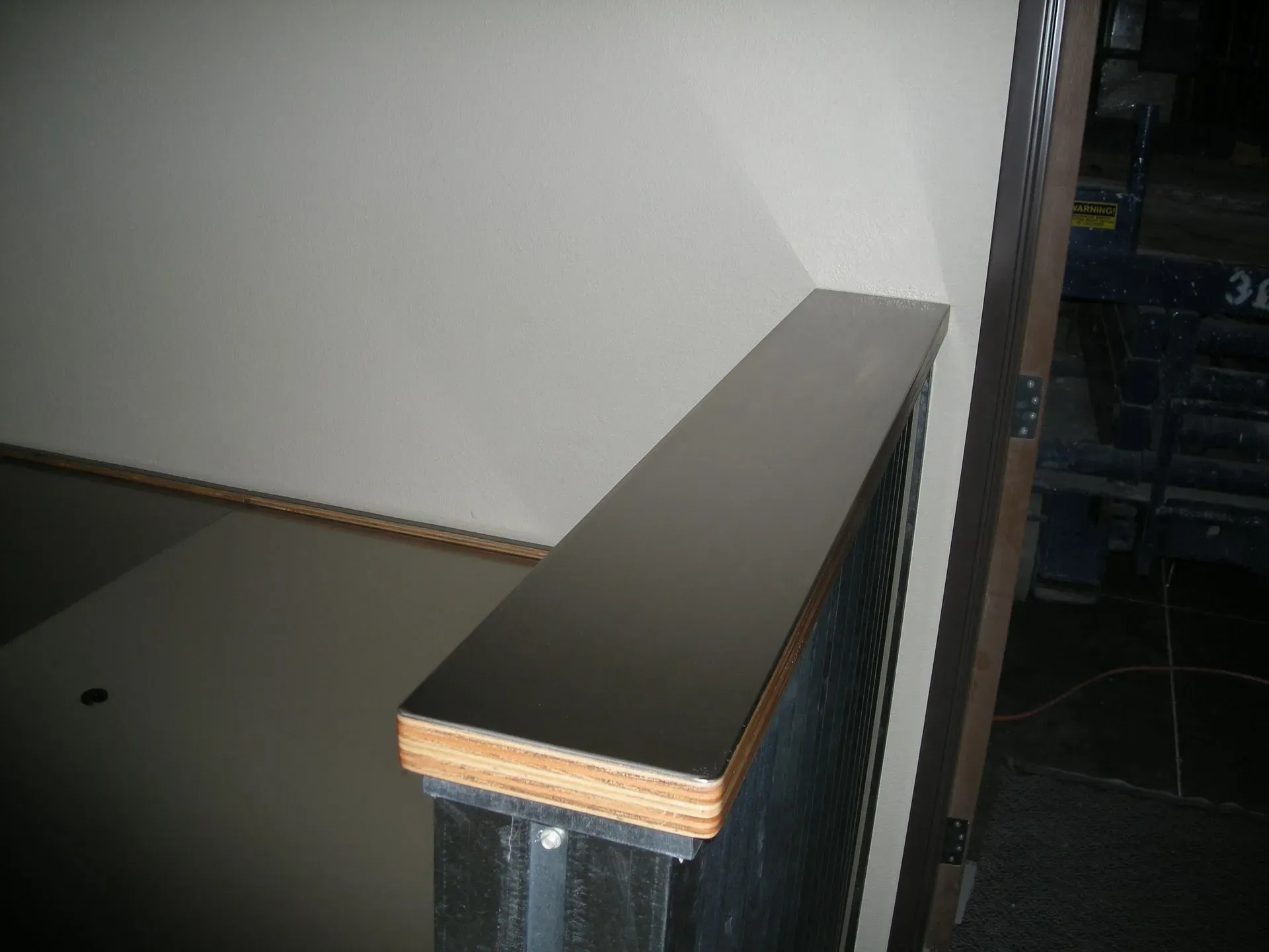 Indoor stair railing with dark wood top and black balusters beside a white wall
