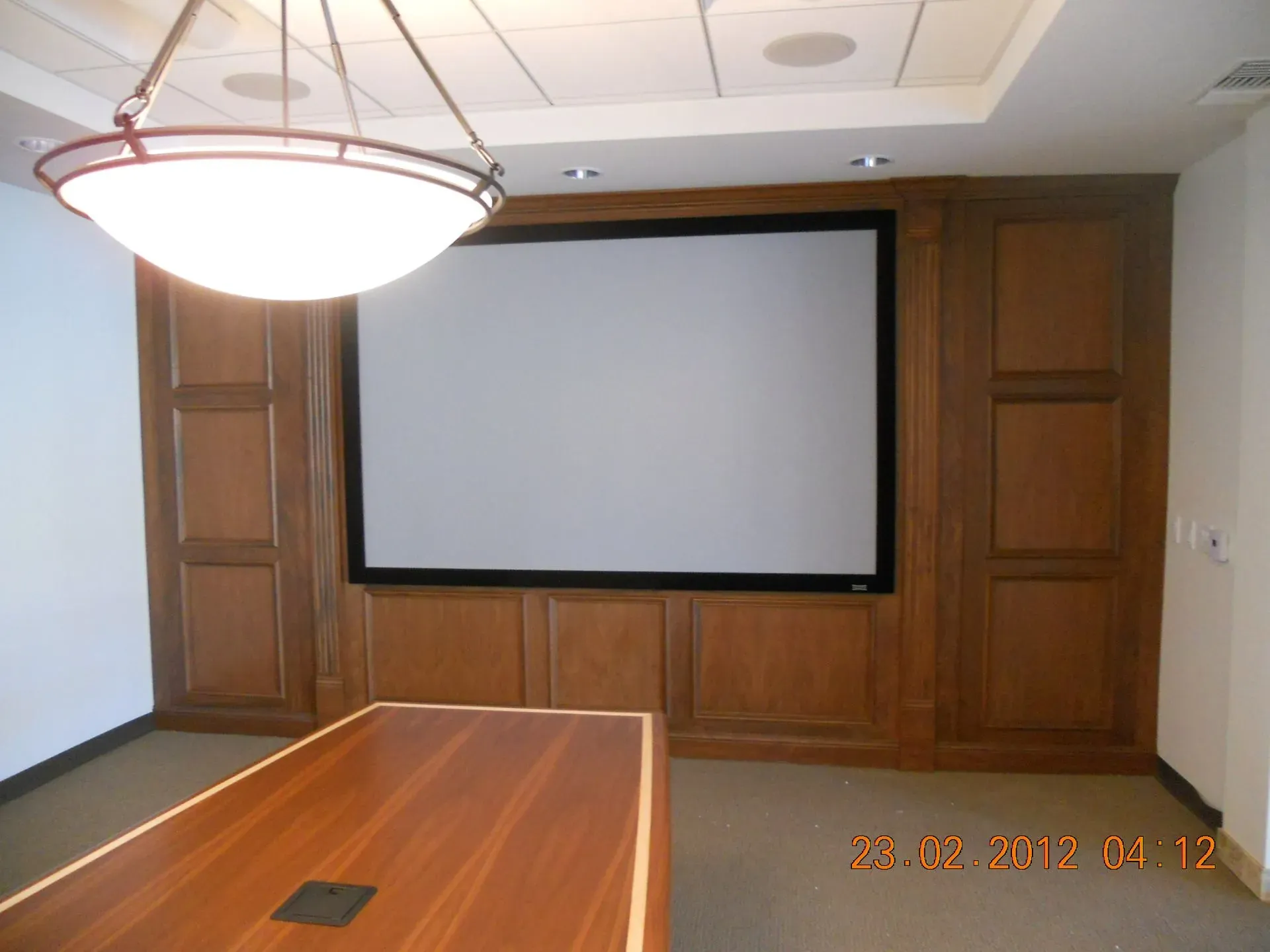 Conference room with a large projection screen, wood-paneled walls, and a long wooden table.
