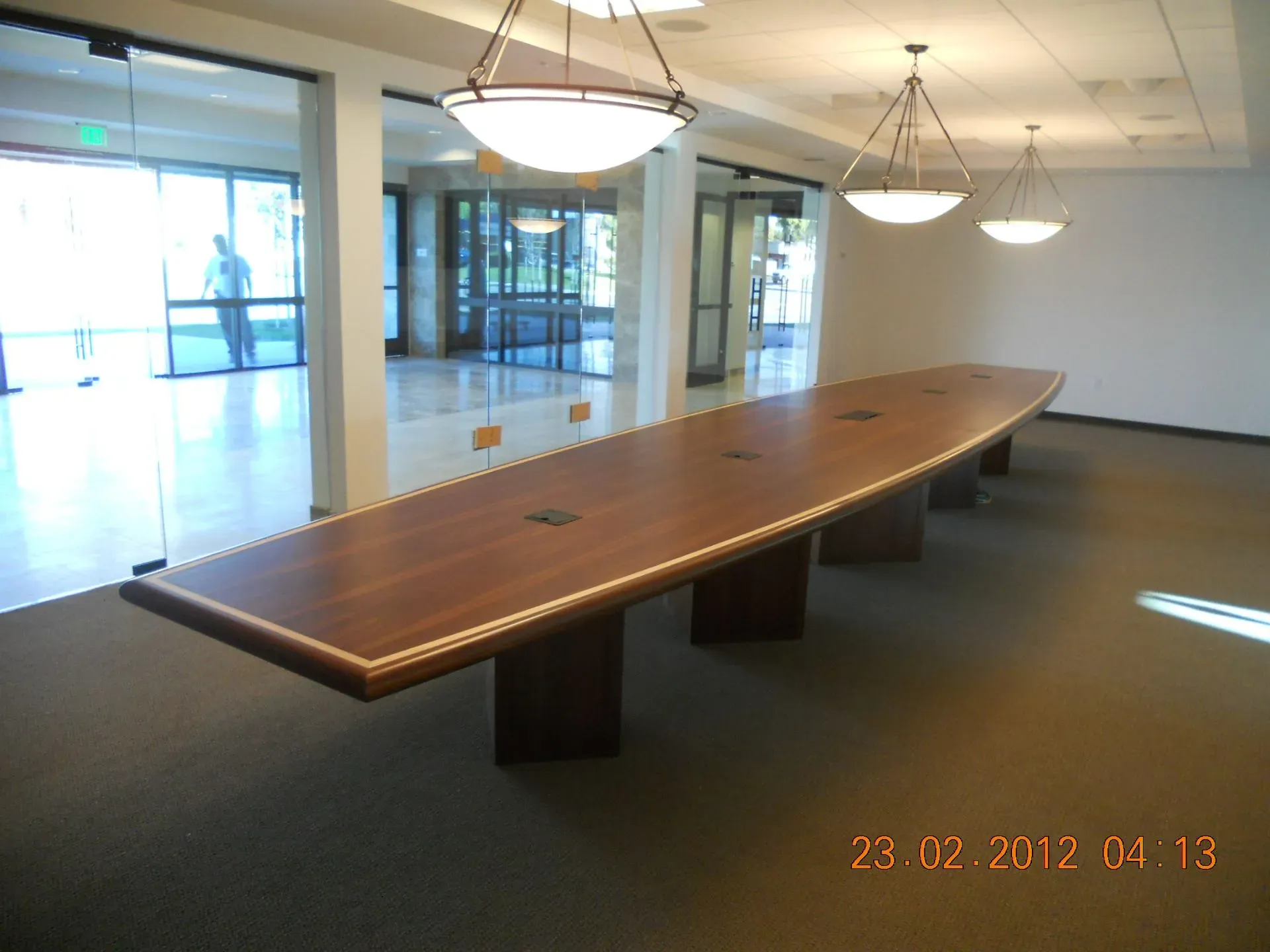 Empty conference room with a long wooden table and hanging lights near glass doors