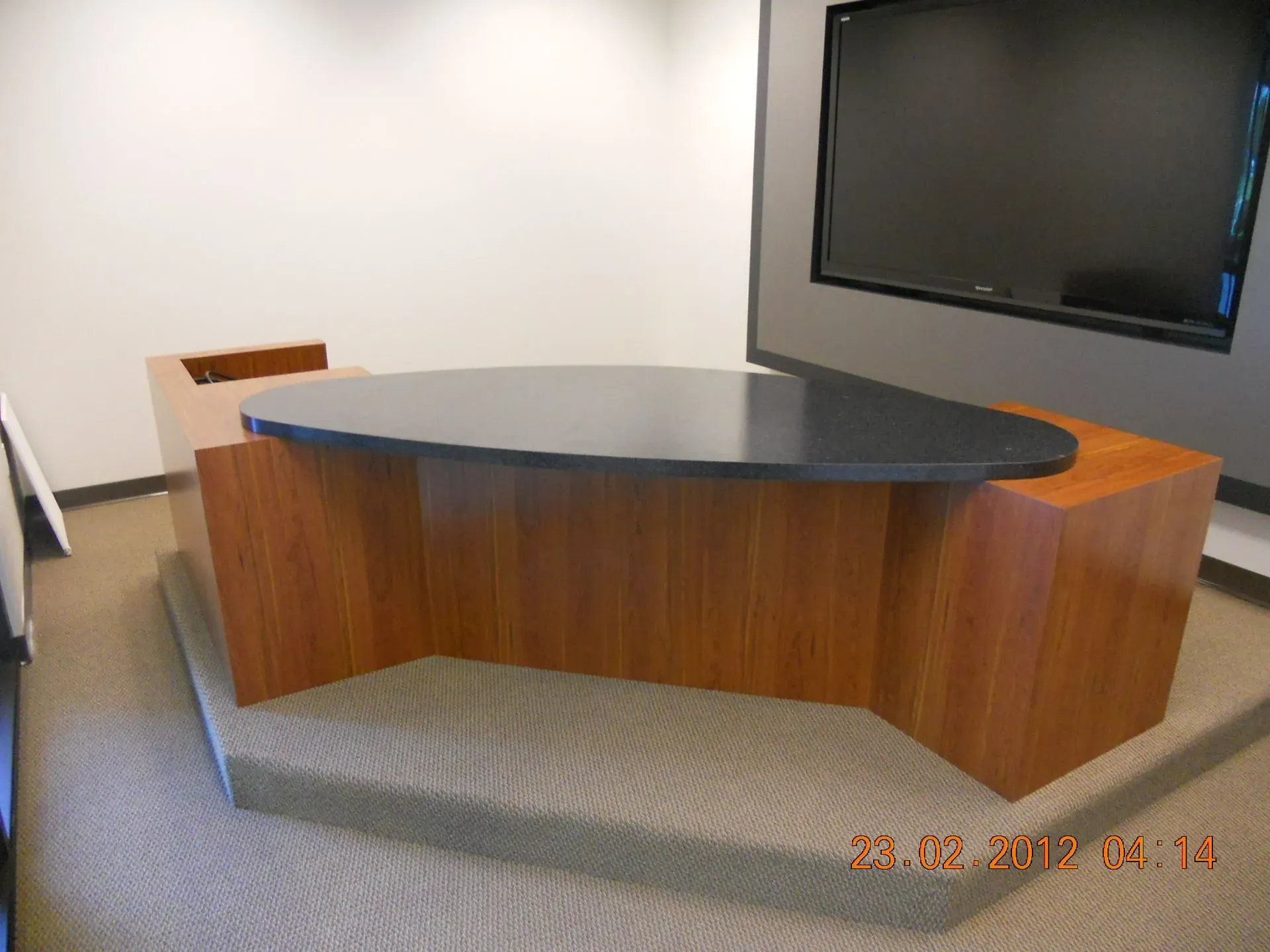 Empty conference room with a curved wooden desk and wall-mounted TV.