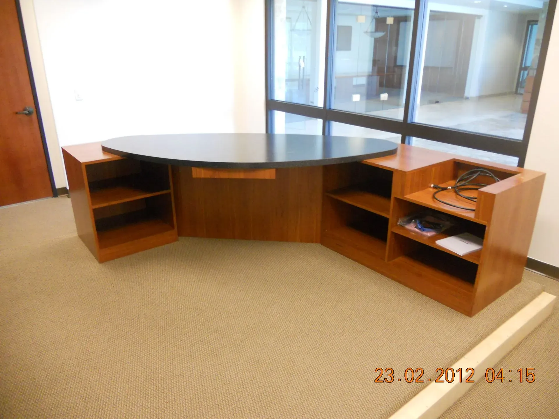 Curved wooden reception desk in an office lobby with beige carpet and glass windows behind it