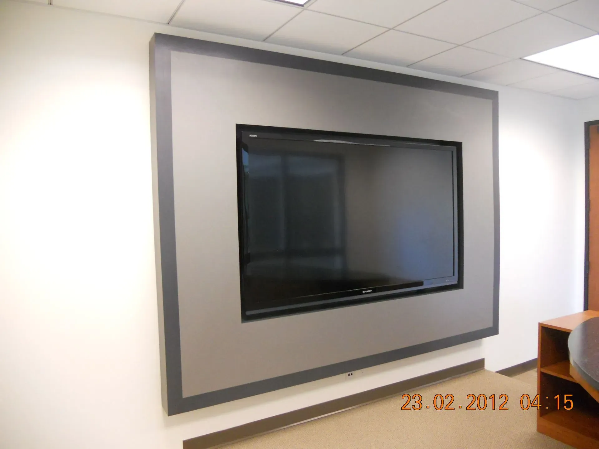 Wall-mounted flat-screen TV on a gray wall in a bright office or conference room