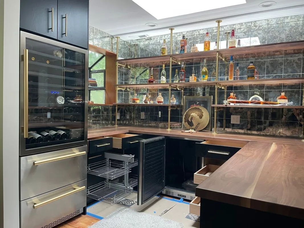 Modern home bar with wine fridge, glass shelves, bottles, and a curved wooden counter