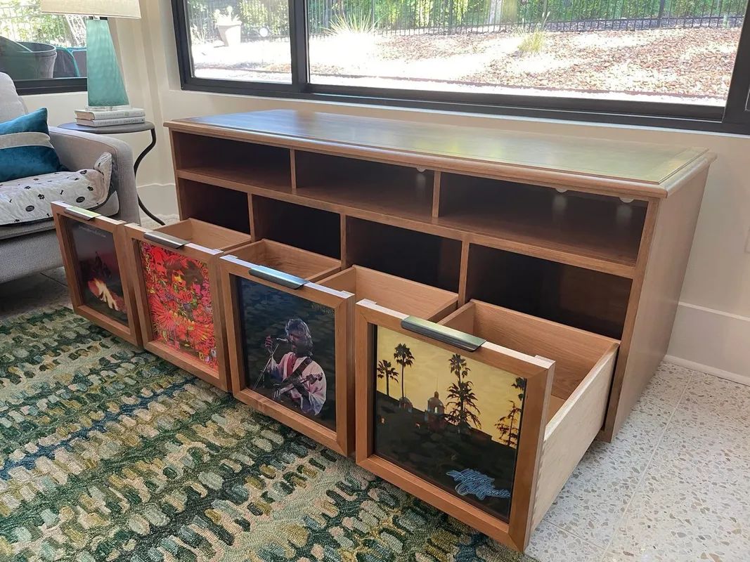 Wooden media console with four framed panels leaning in front, beside a window on a patterned rug.