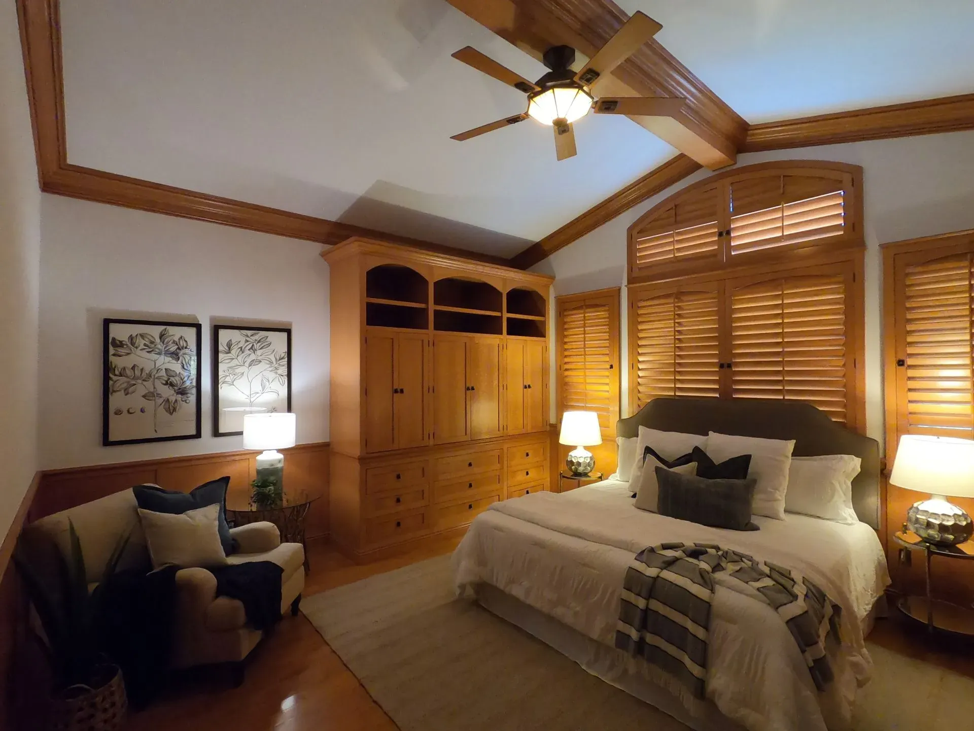 Cozy bedroom with a bed, wooden armoire, armchair, ceiling fan, and shuttered windows