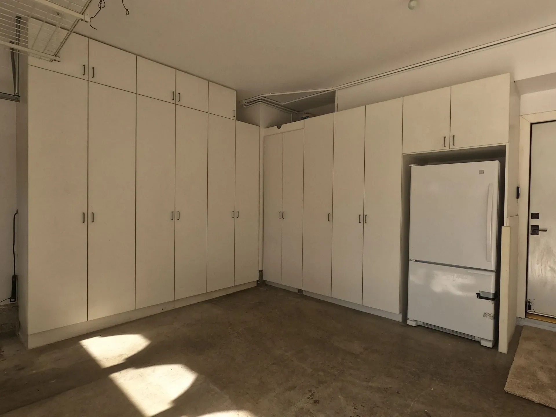 White built-in closet cabinets line a bare room with a concrete floor and sunlight on the floor.