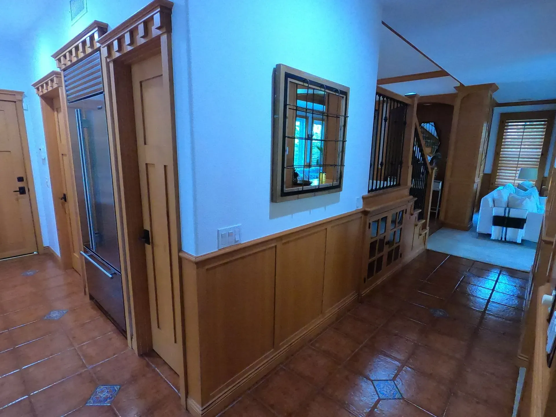 Hallway with terracotta tile floor, wood paneling, mirrored wall, and staircase in the background.