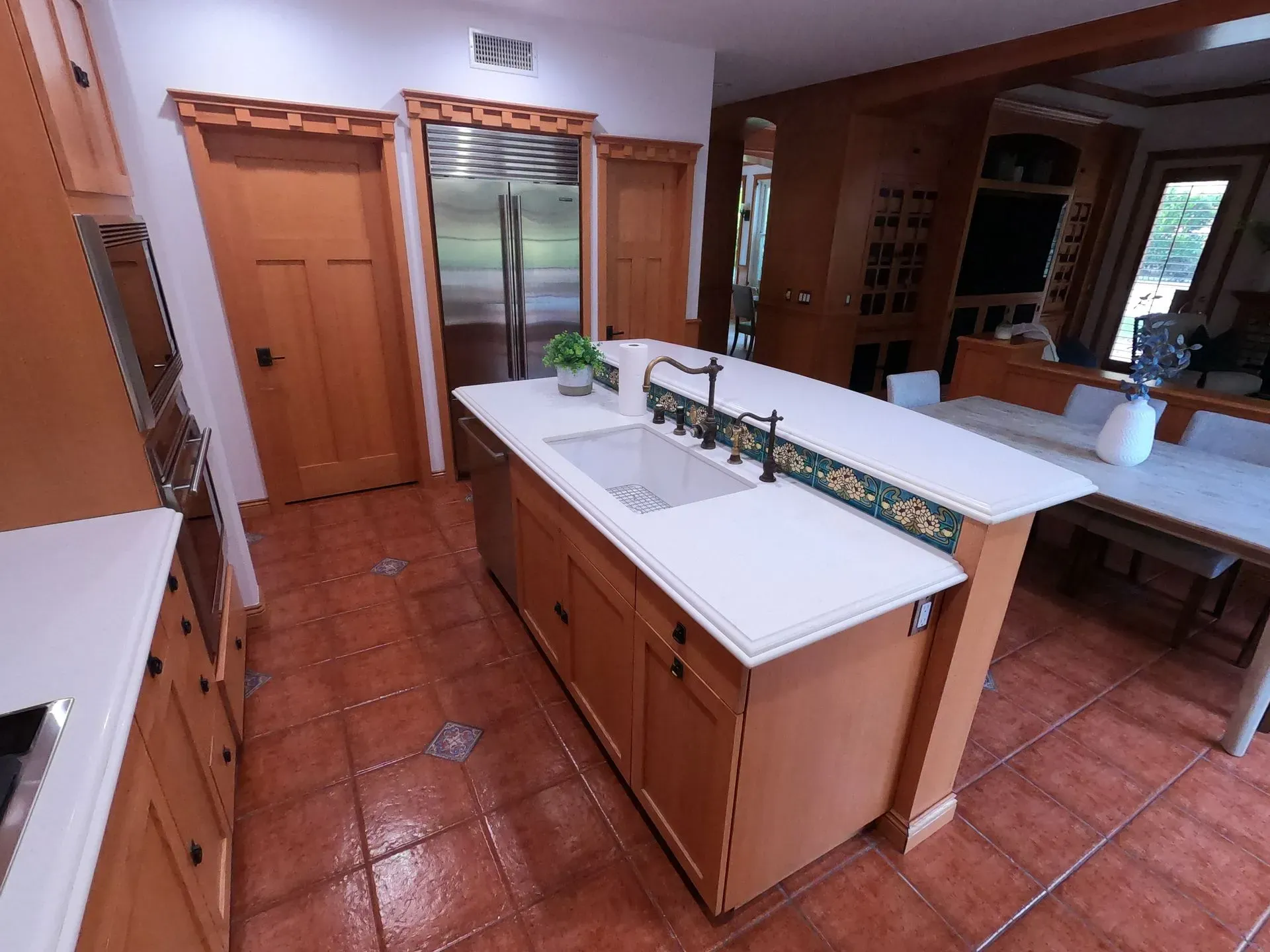 Modern kitchen with terracotta tile floors, wood cabinets, white island, and stainless appliances