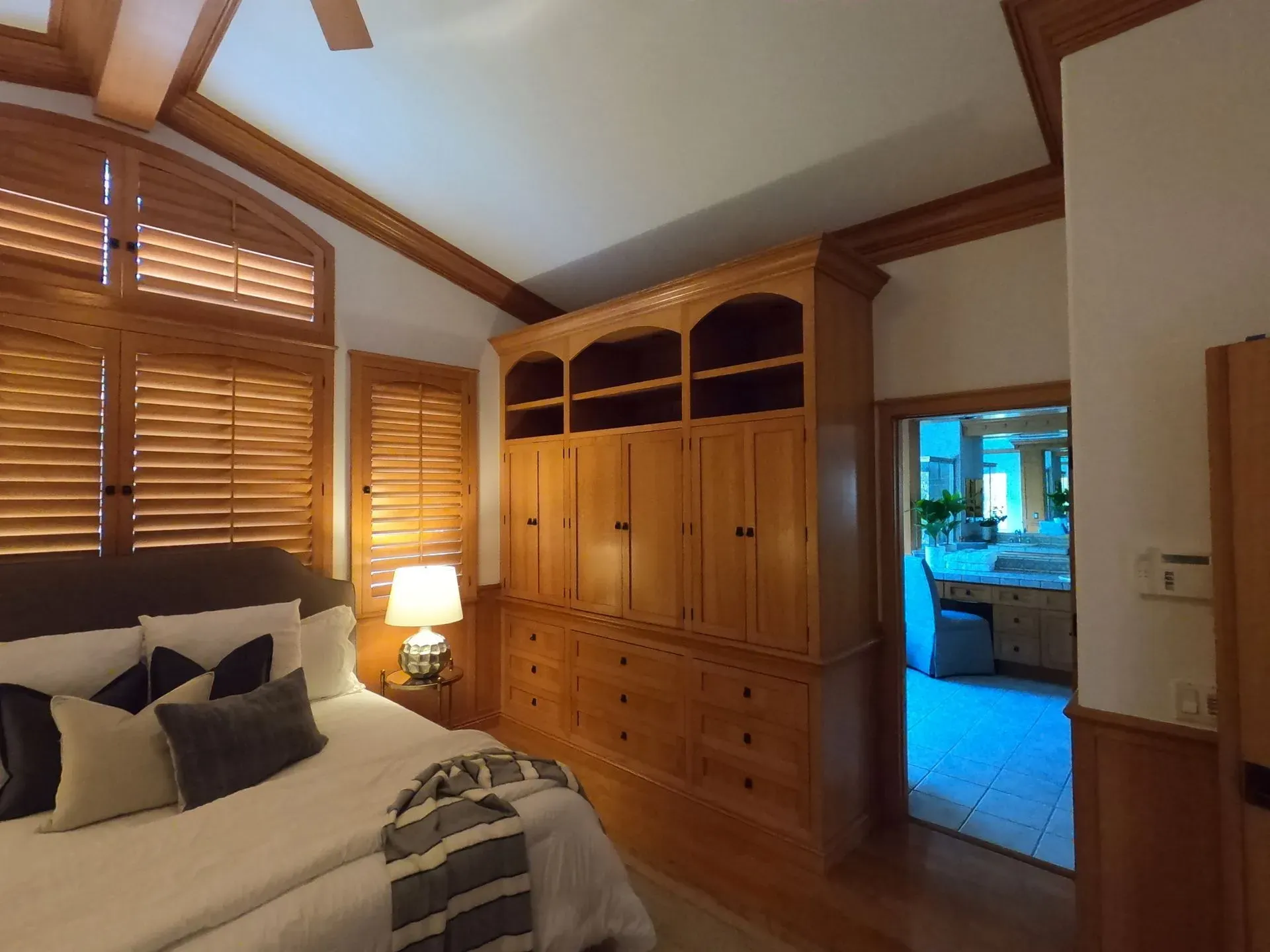 Bedroom with wood-paneled walls, a large bed, built-in dresser, and open doorway to a lit bathroom