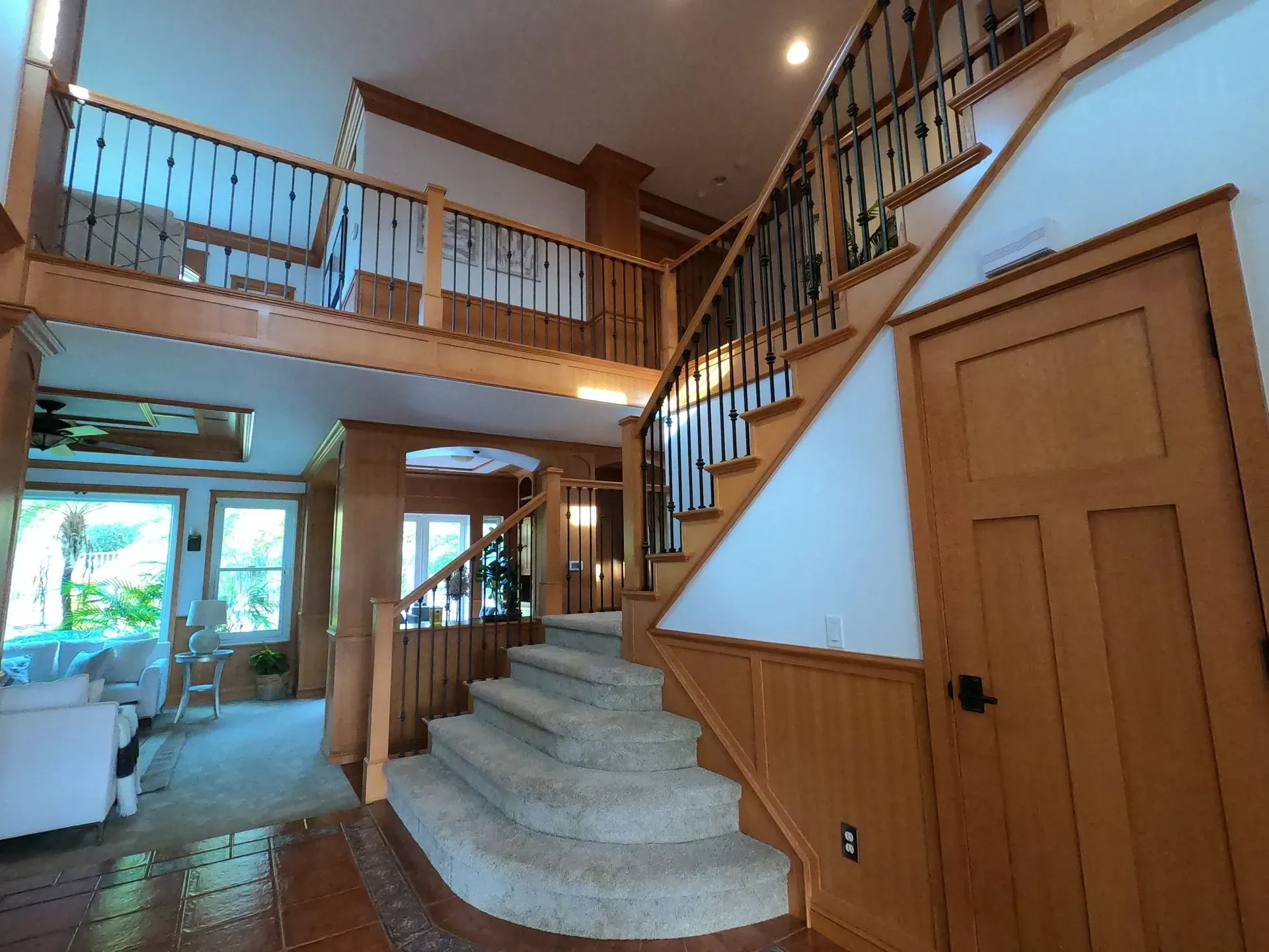 Bright foyer with curved staircase, wood railing, and loft balcony in a sunlit home