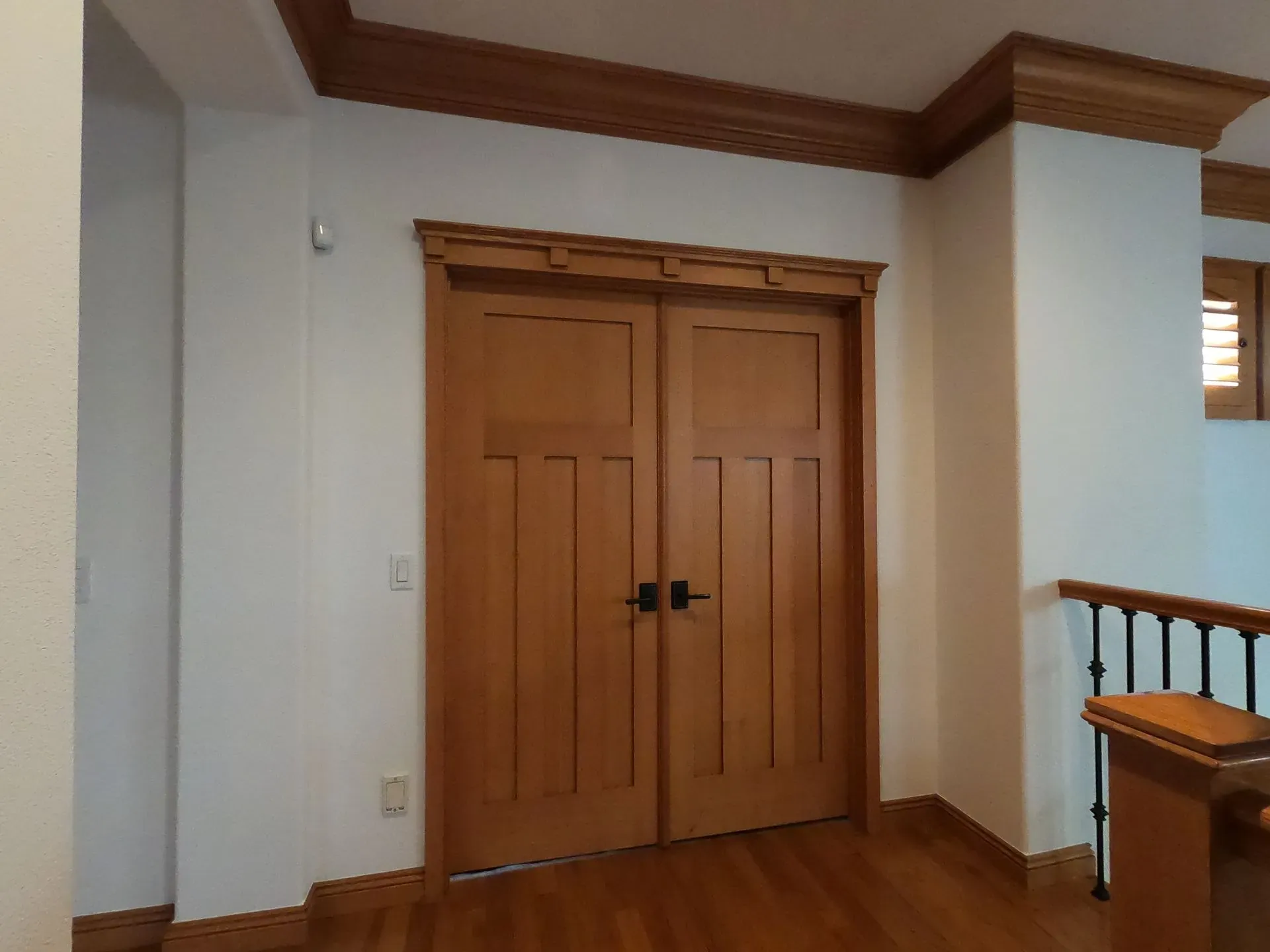 Wooden double doors in a hallway with white walls and brown trim