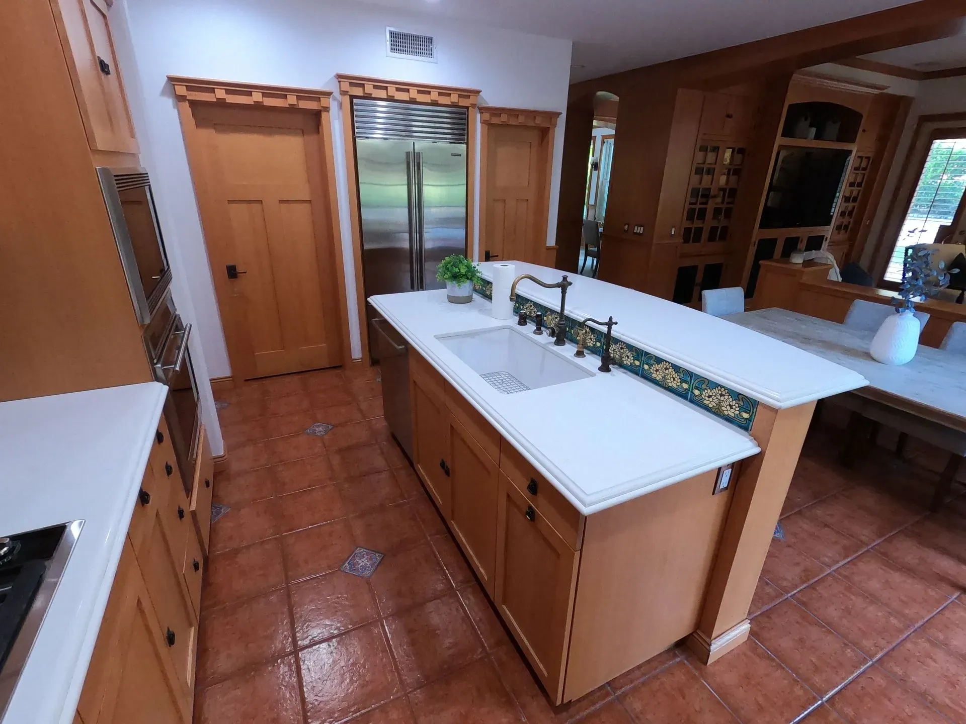 Kitchen with wooden cabinets, white countertops, stainless refrigerator, and central island on terracotta tile floor