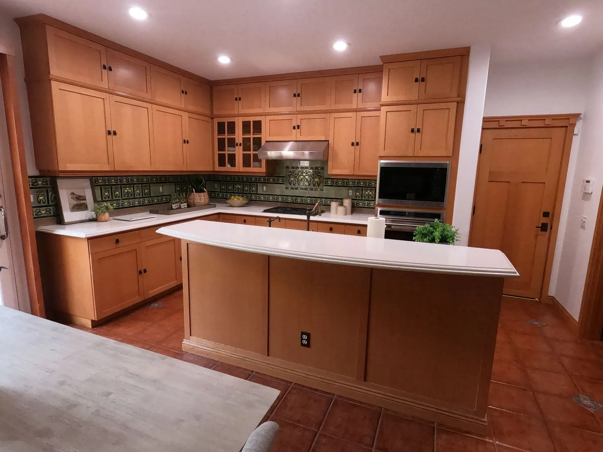 Empty kitchen with light wood cabinets, white island, and stainless steel appliances under recessed lighting