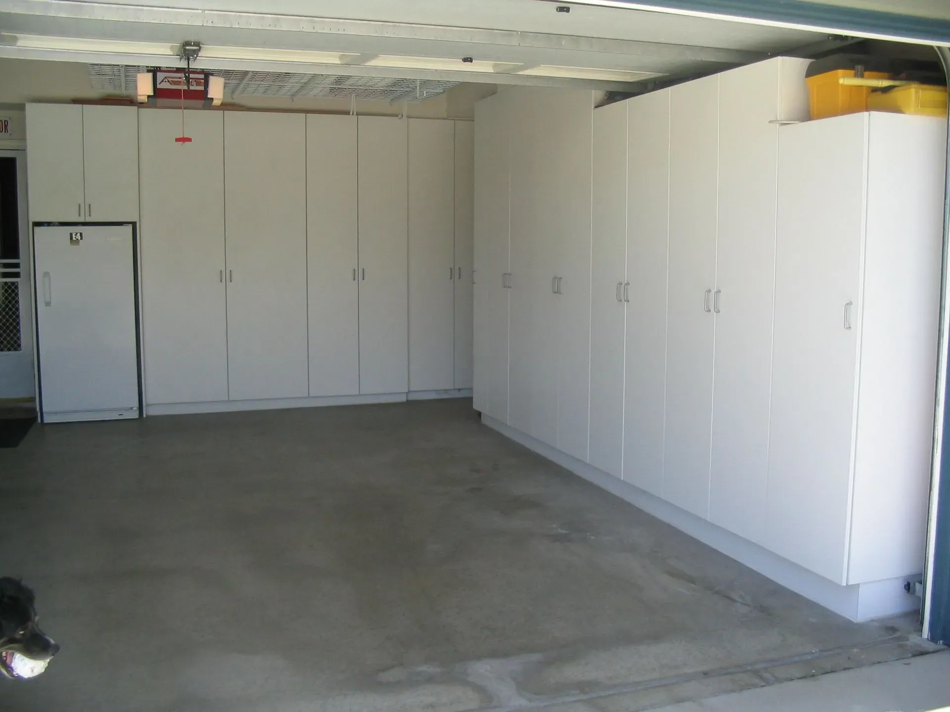 Empty garage with white storage cabinets lining the walls and a concrete floor.