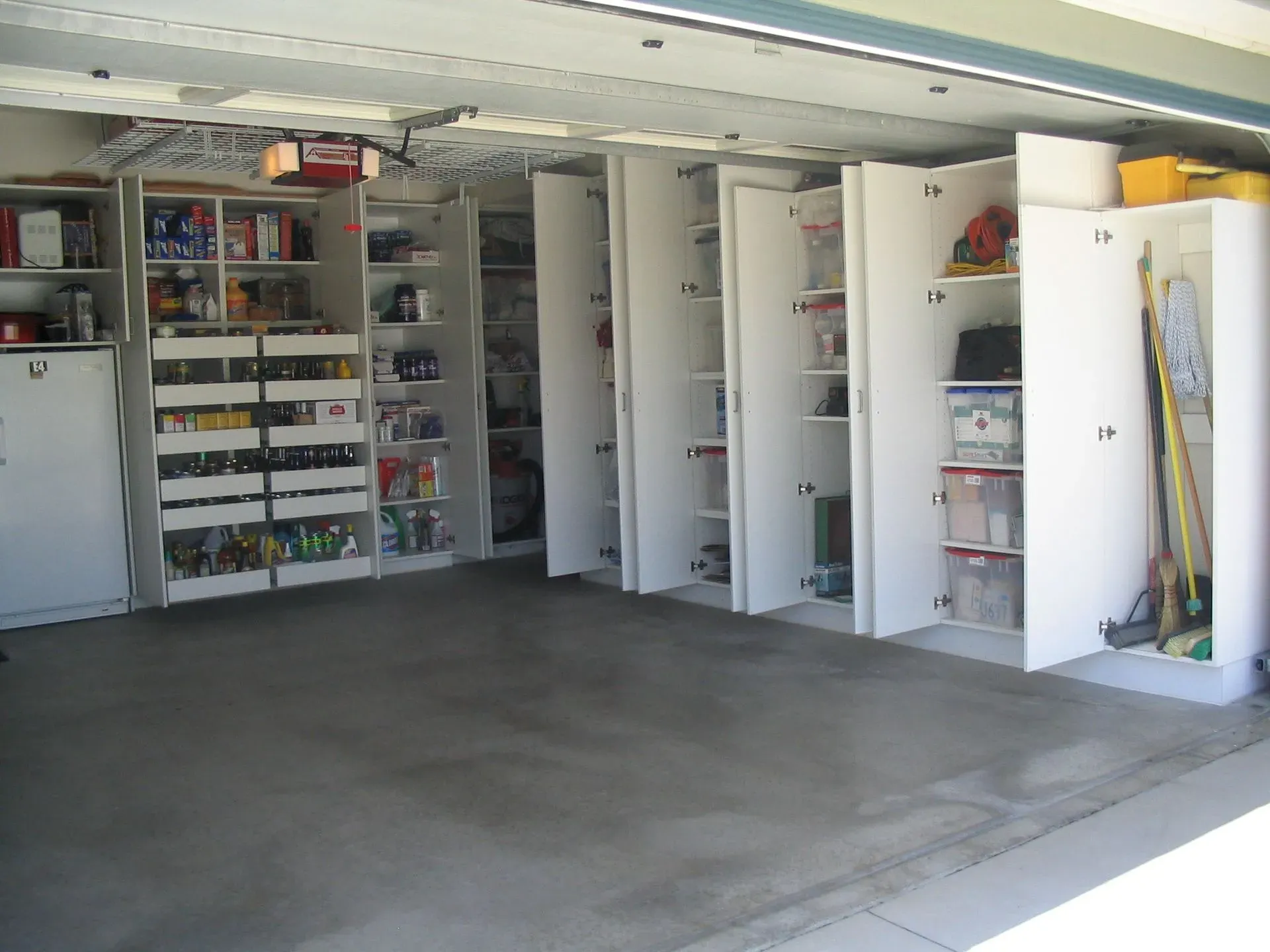 Open garage with white storage cabinets, shelves, and a concrete floor