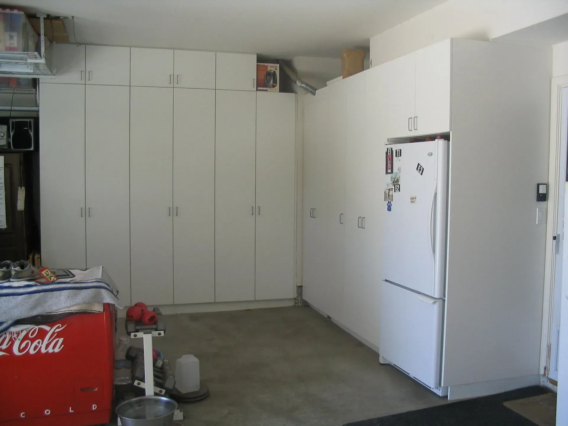 Garage with white cabinets and a refrigerator; red Coca-Cola cooler in the foreground.