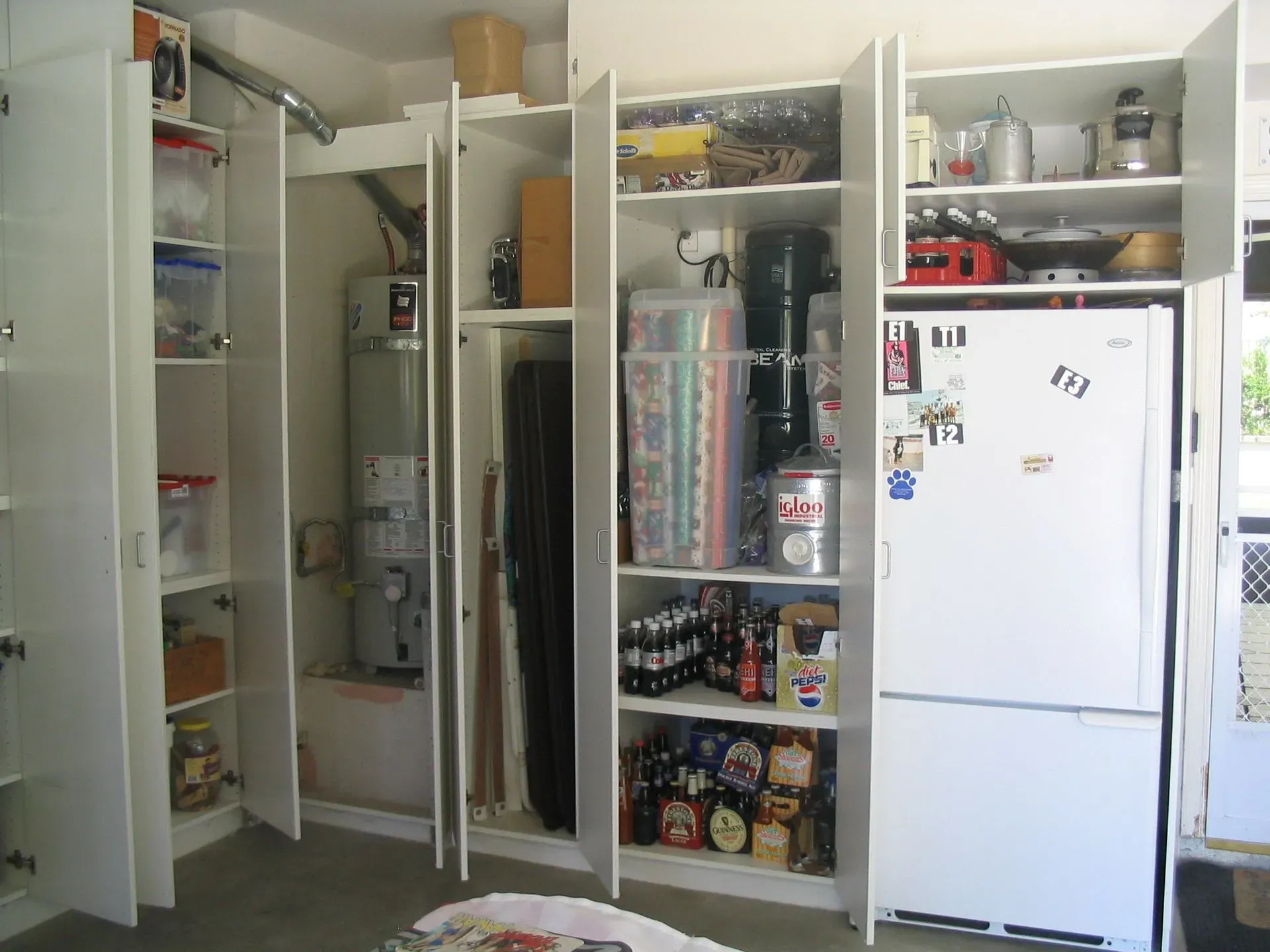 Open pantry with shelves of food, appliances, and a white refrigerator.