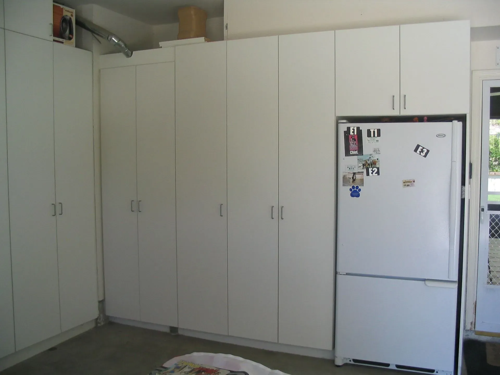 Small kitchen with tall white cabinets and a white refrigerator covered in magnets.