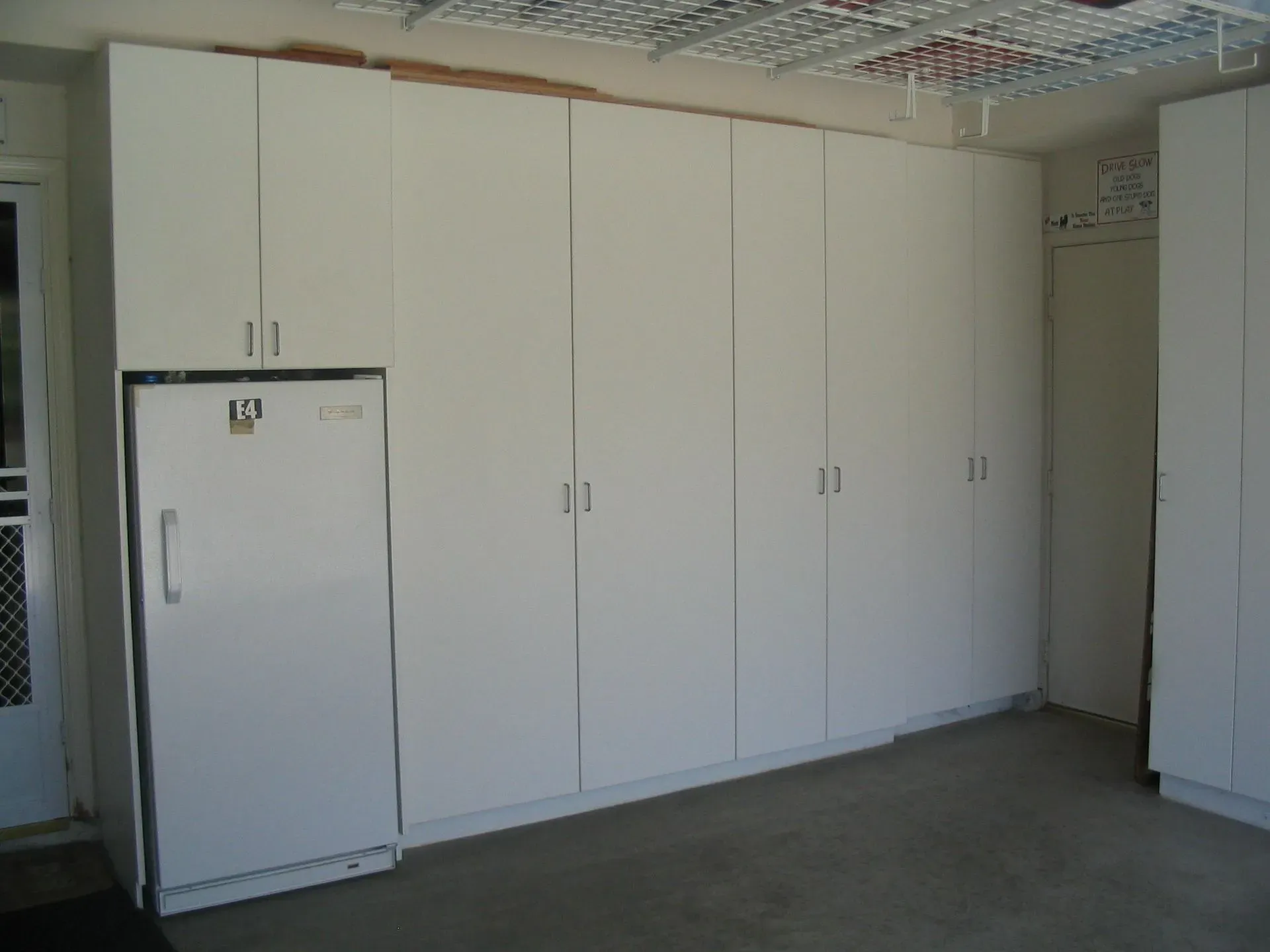 White storage cabinets and a small fridge in a plain room with a gray floor and ceiling grid