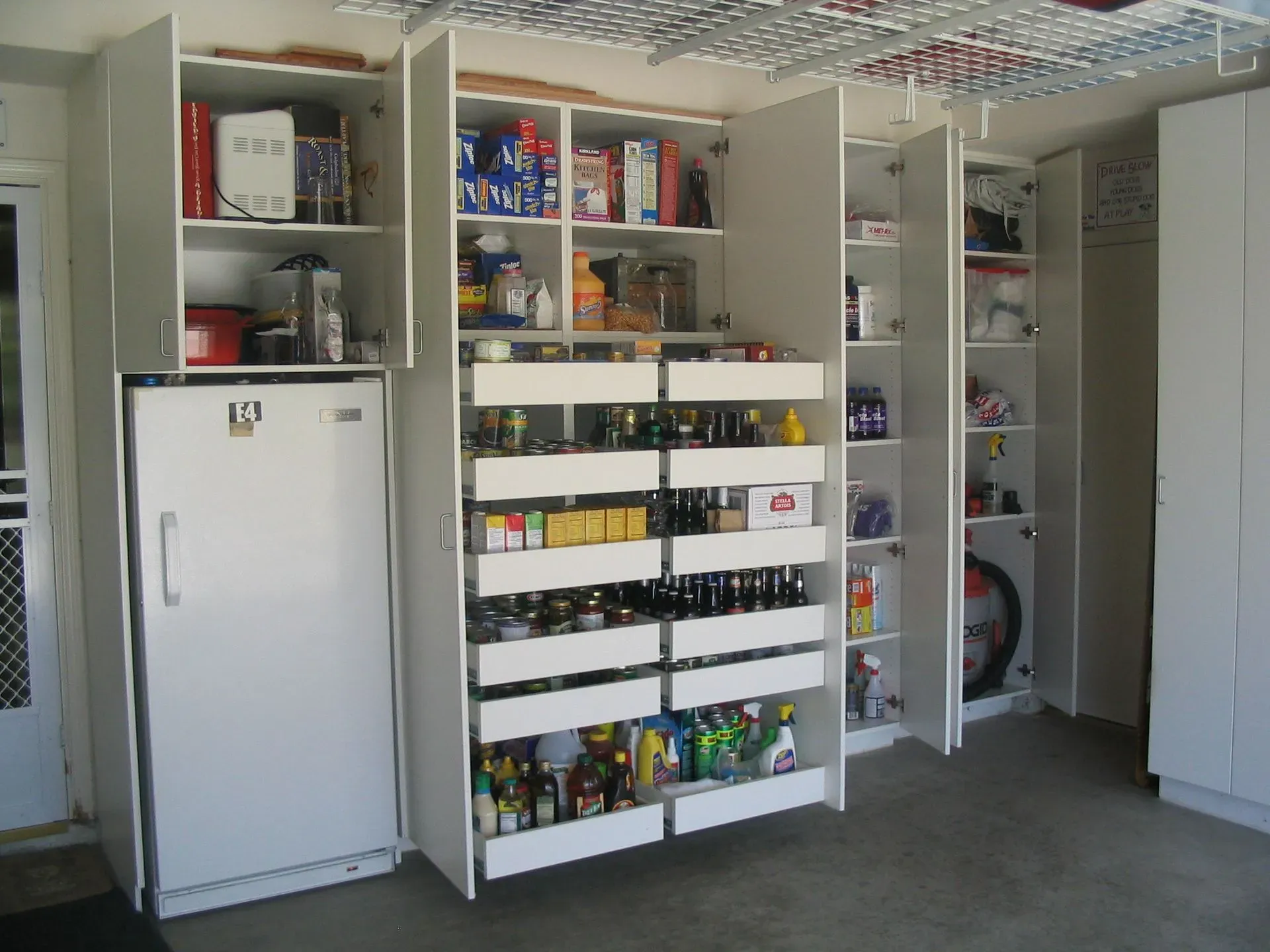 Open pantry with white cabinets, shelves of snacks and supplies, and a small refrigerator.