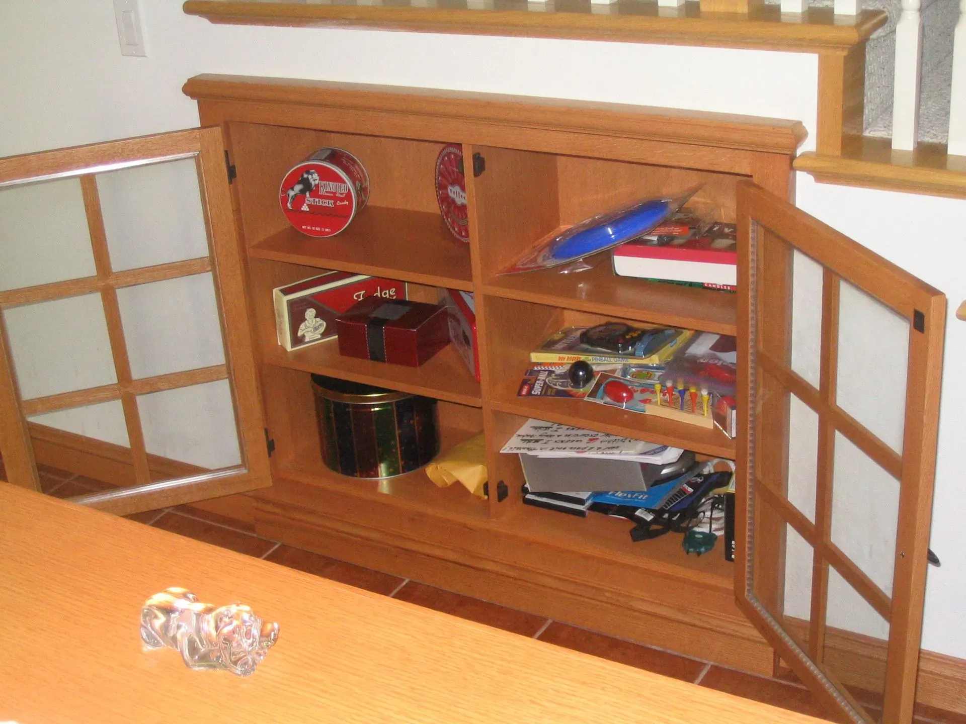 Open wooden cabinet with shelves and papers in a room; small crumpled object on the floor nearby