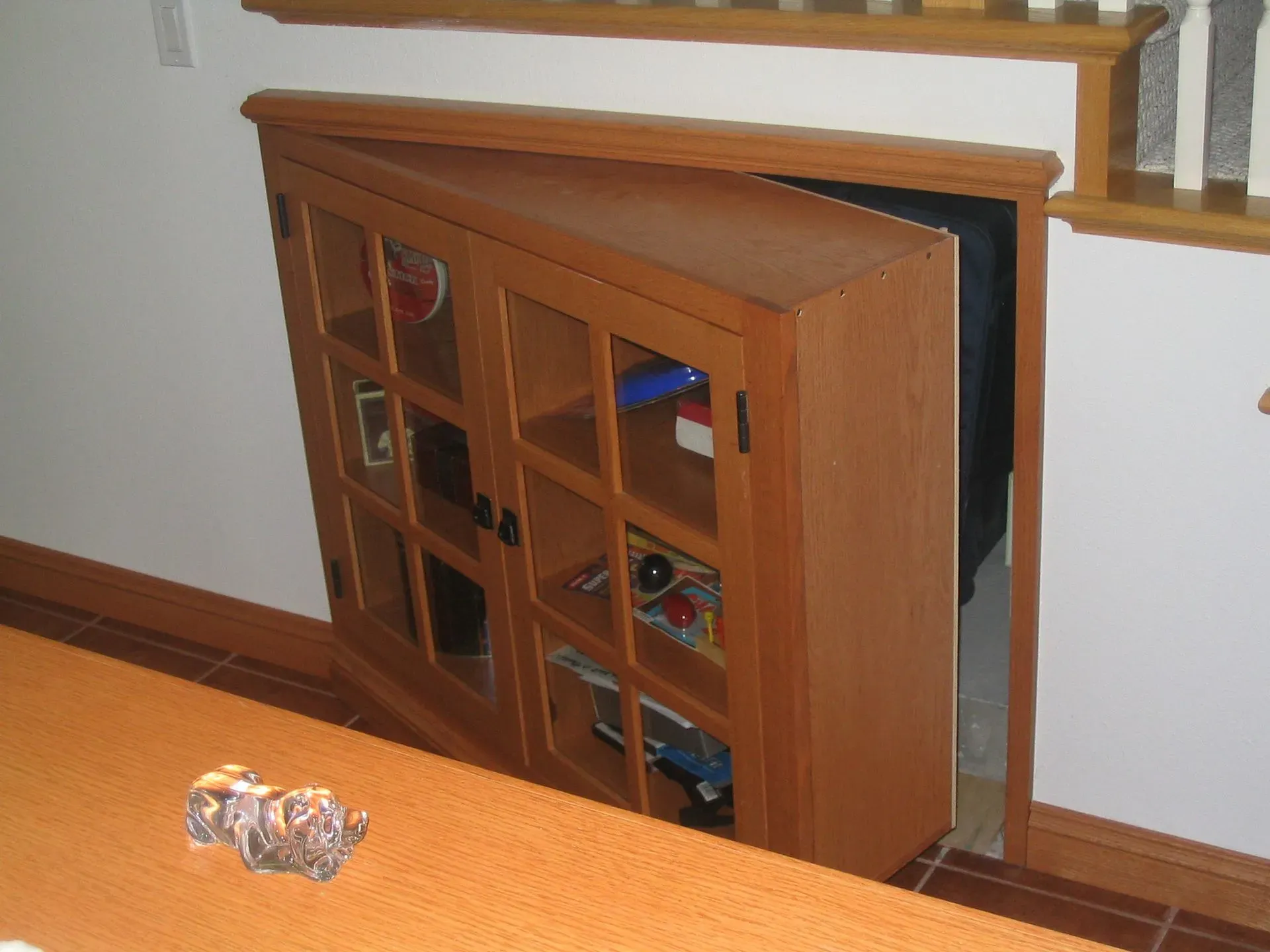 Wooden cabinet tucked under a staircase beside a railing, with glass-paneled doors.