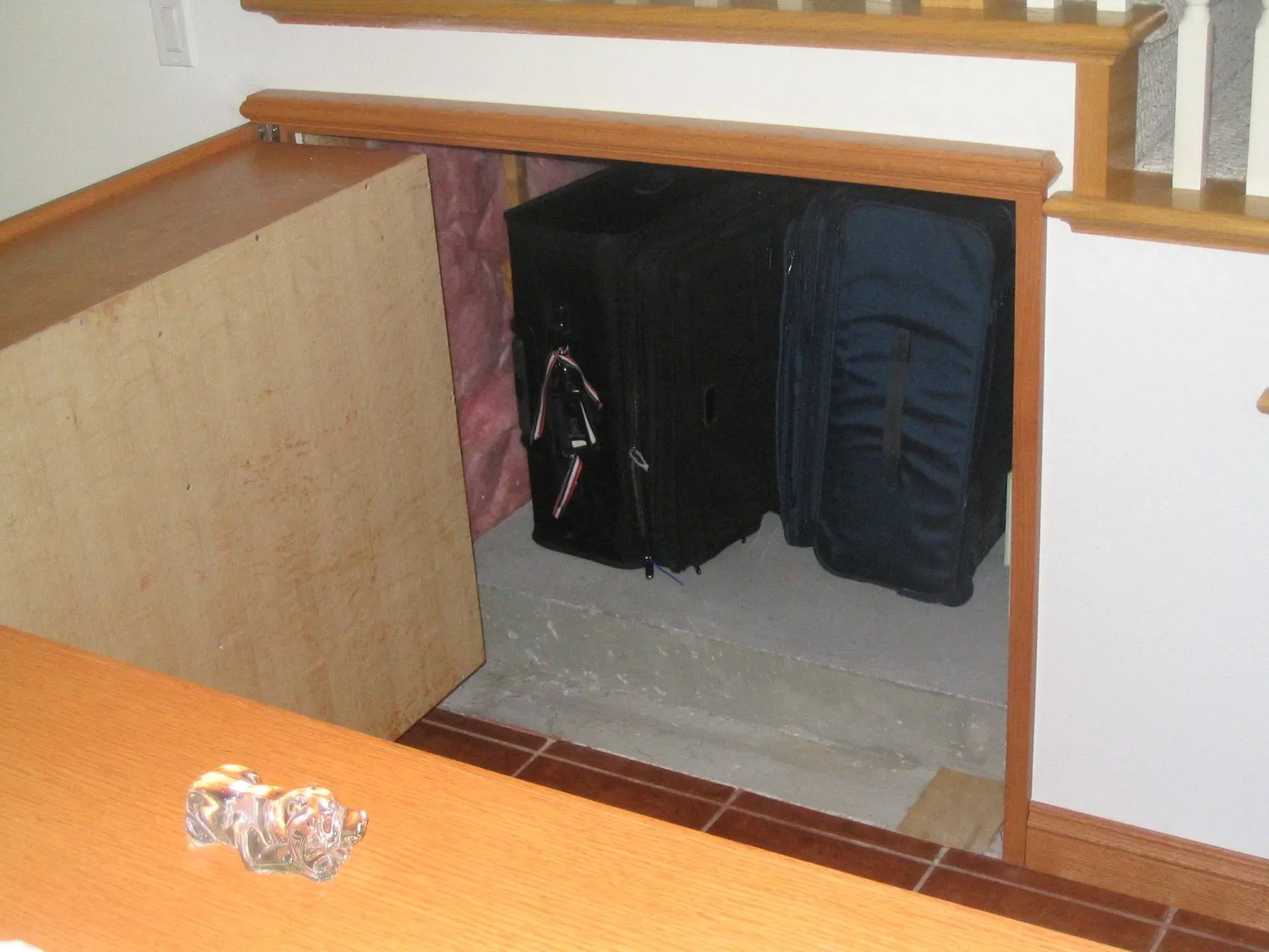 Basement stairwell with a small closet-like opening under a wooden railing and a black bag inside.
