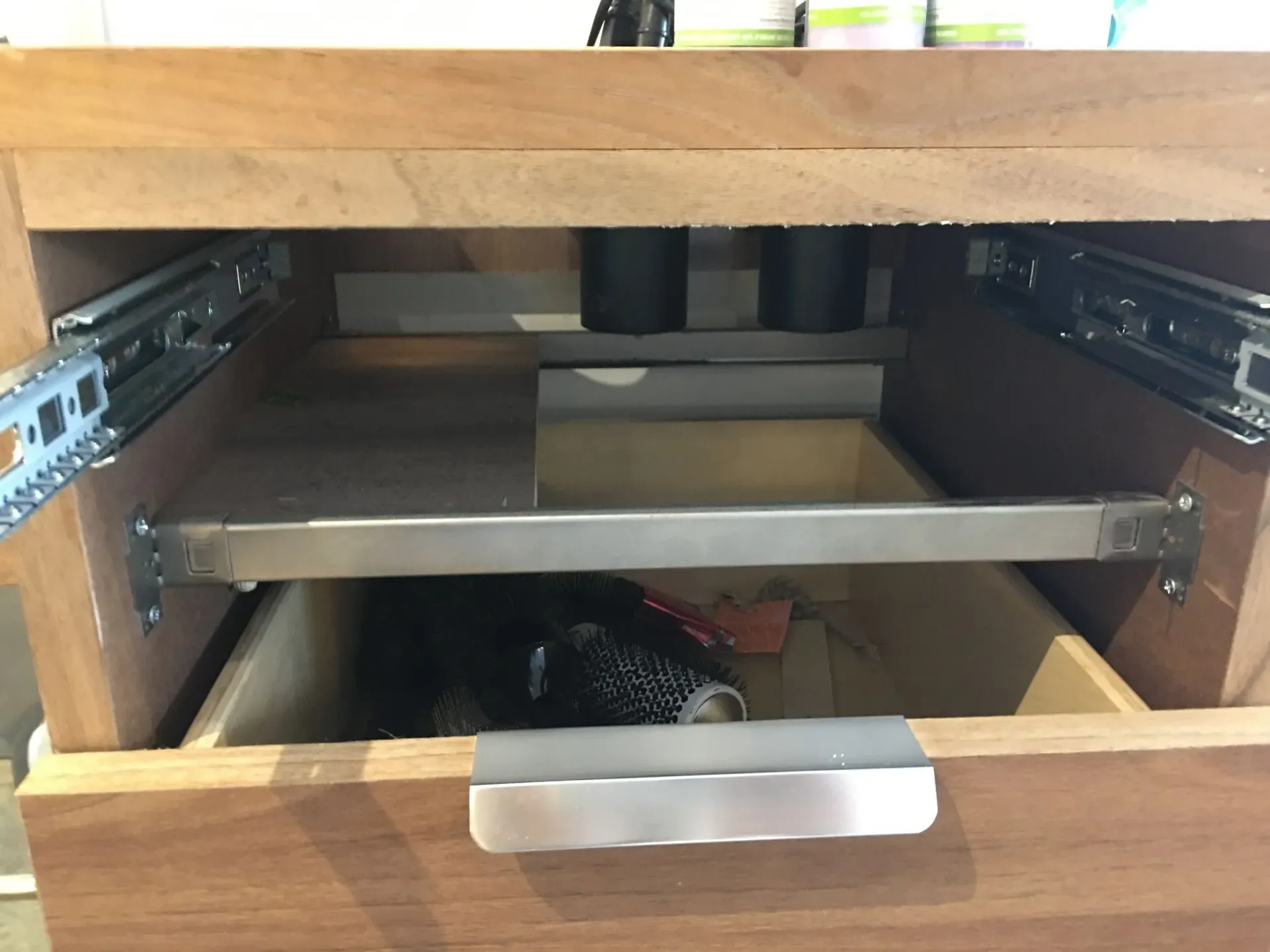 Open kitchen drawer with metal sliding shelf and drawer slides visible inside wooden cabinet