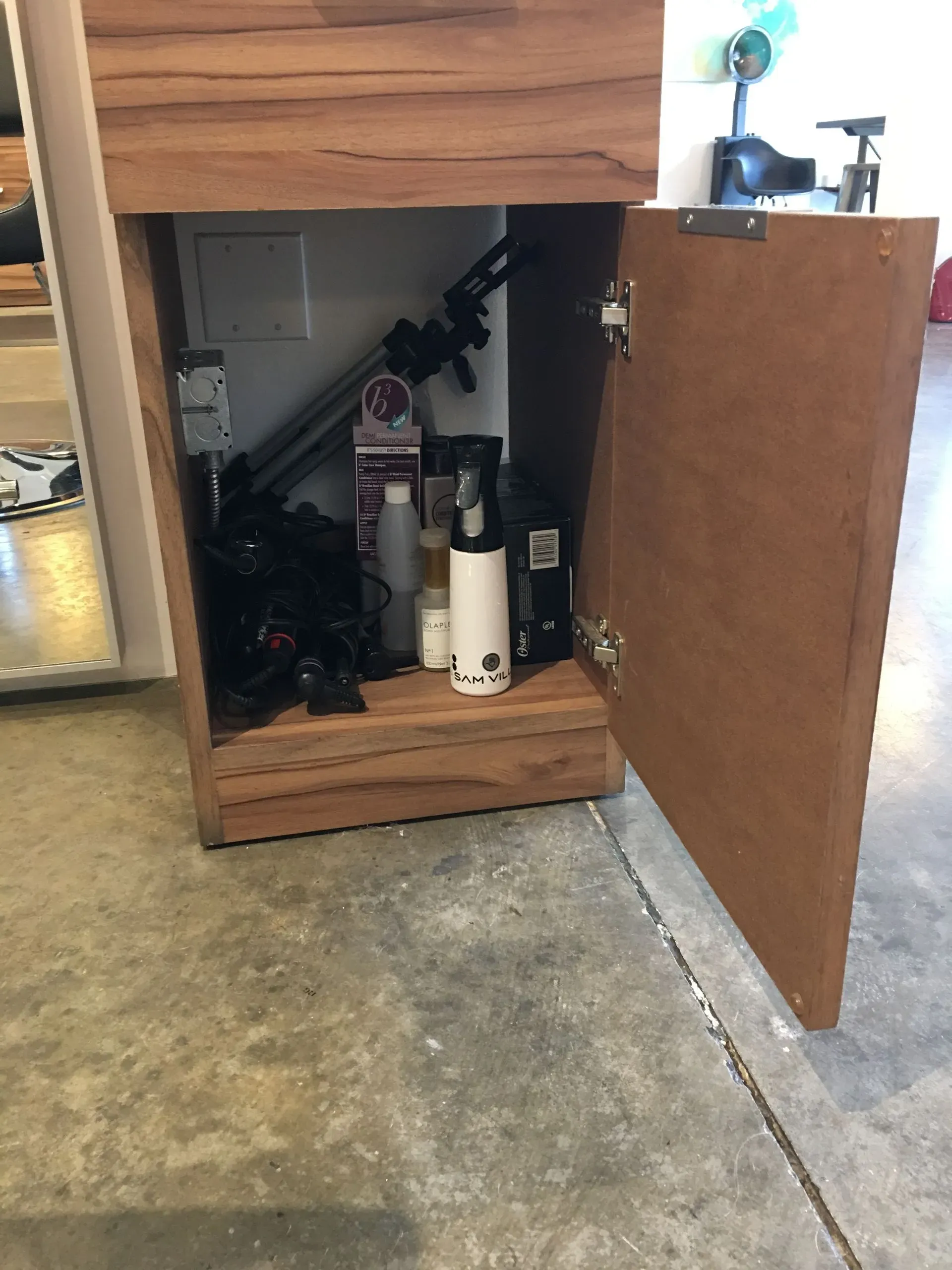 Open cabinet under a workbench with fire extinguishers and tools inside; door open in a garage.