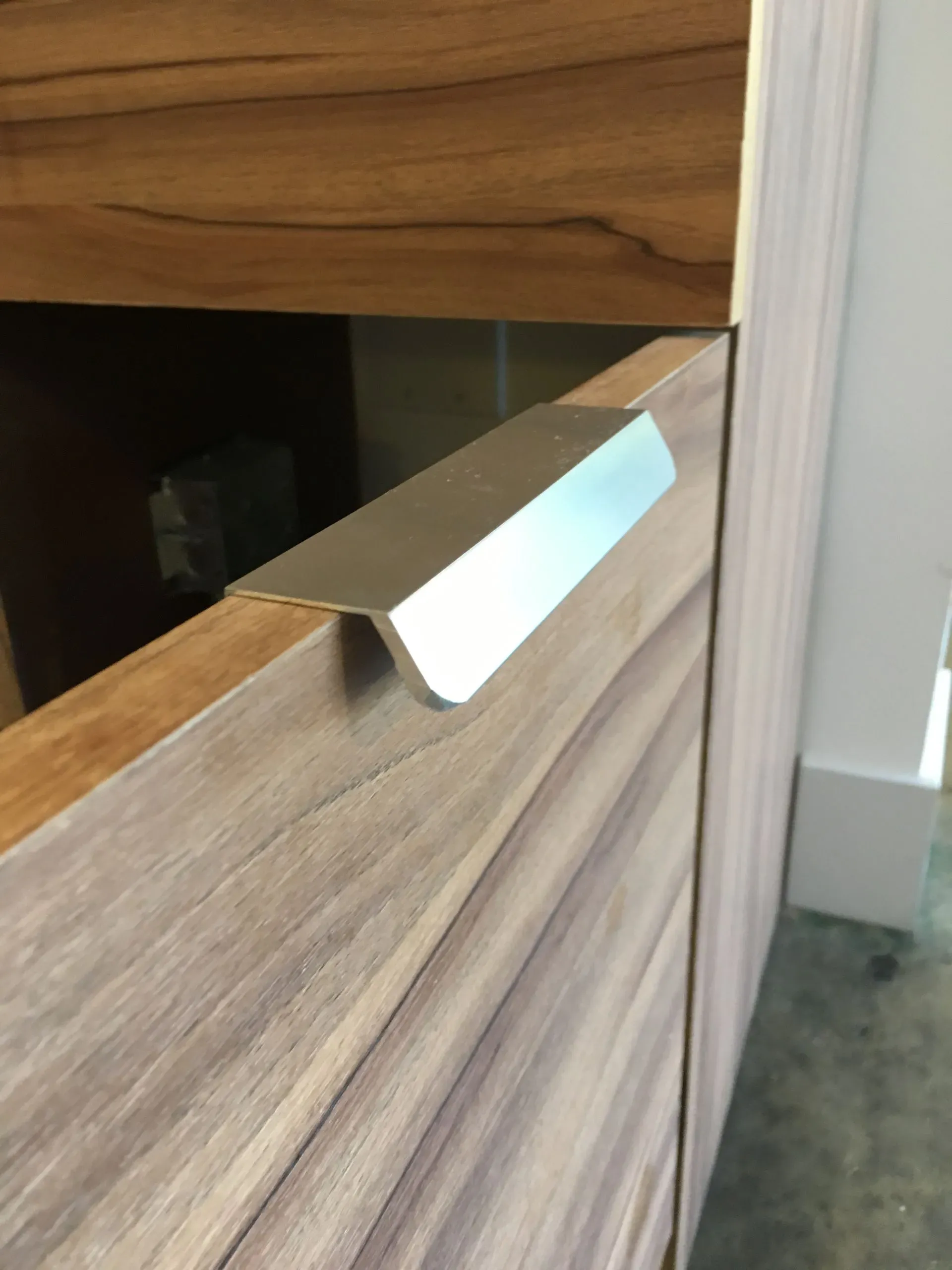 Chrome pull handle on a light wood cabinet or drawer front.