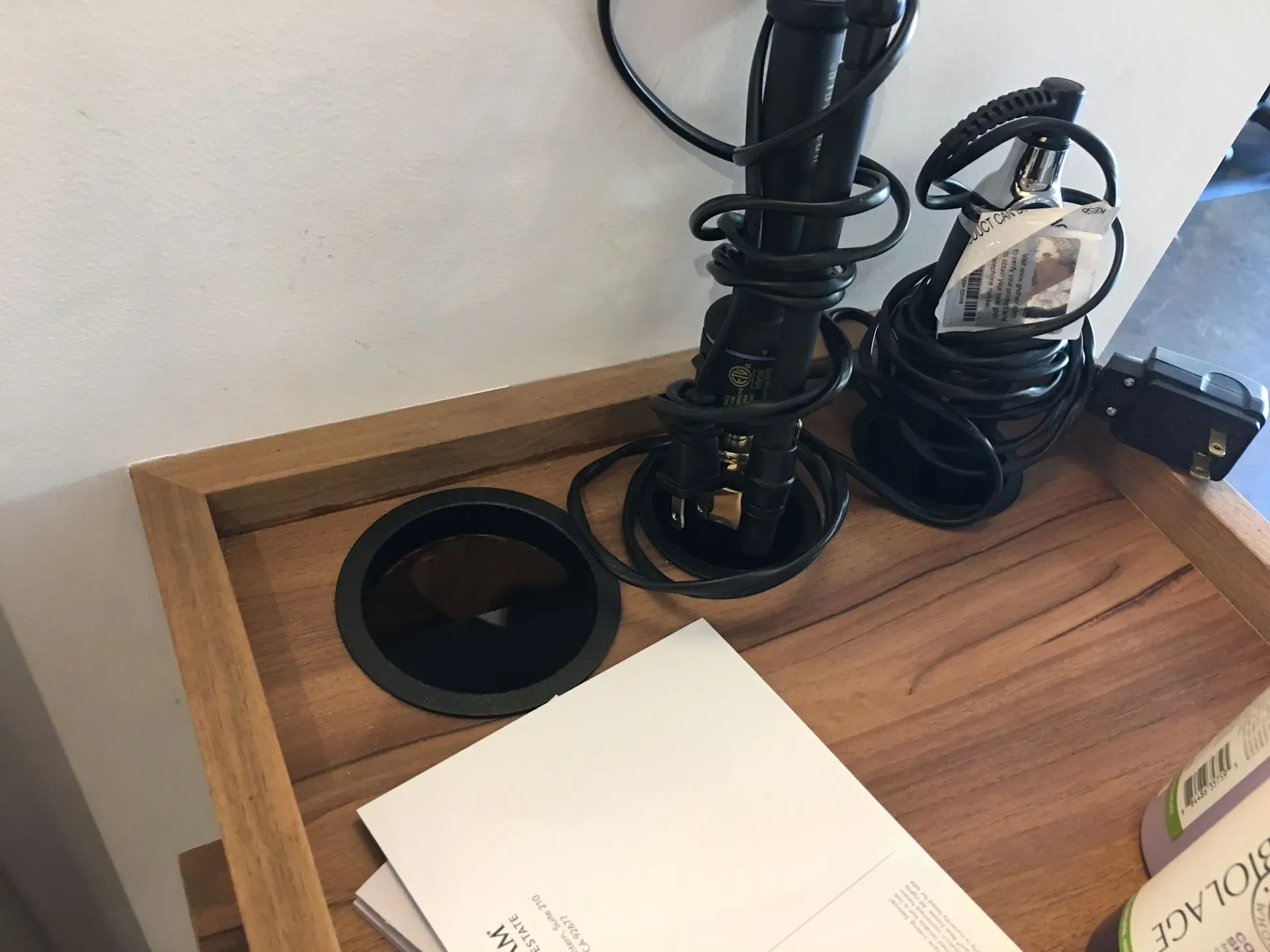 Wooden desk with cable grommet holes, black cords, and papers on the surface