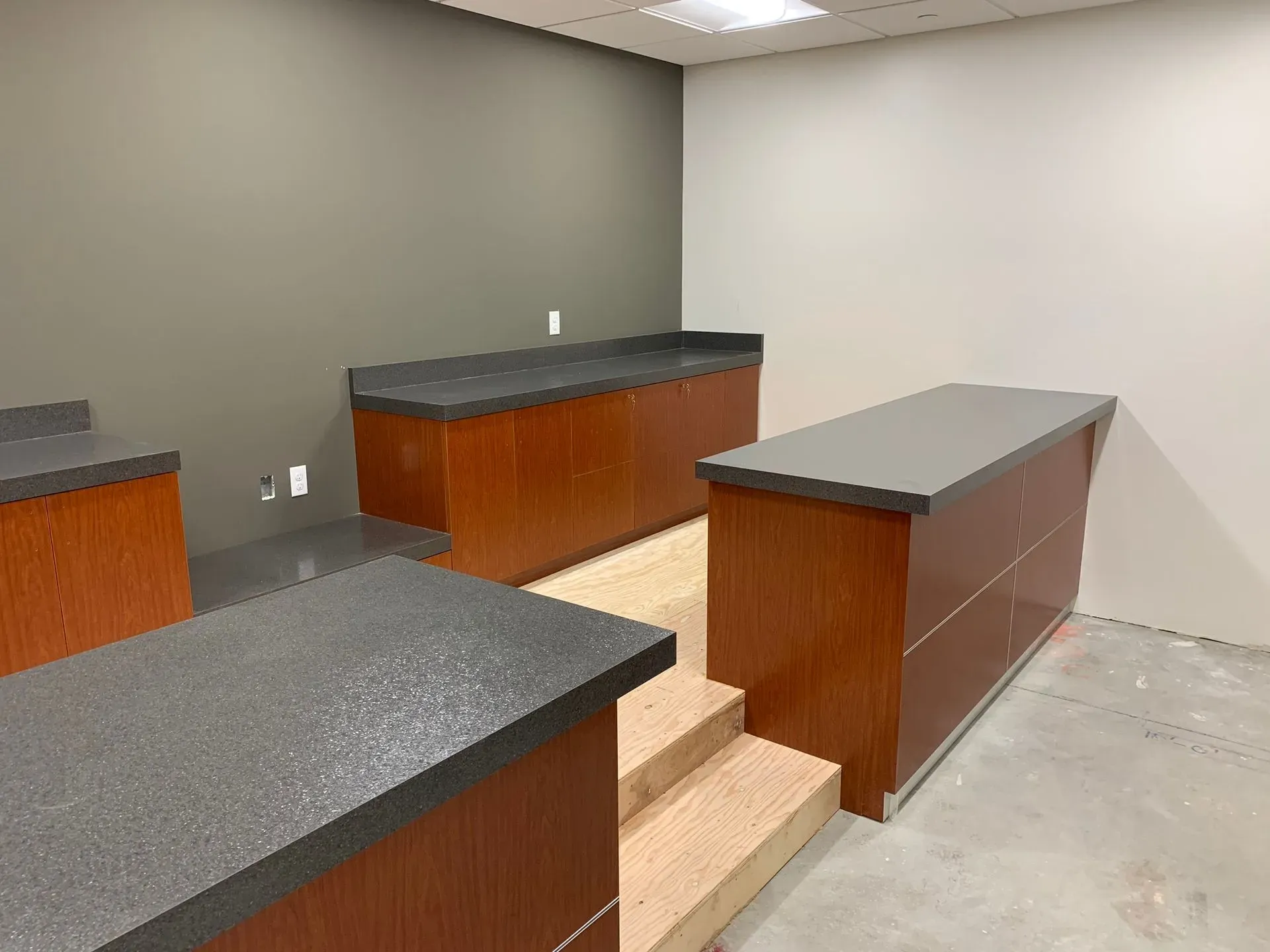 Empty kitchen with gray countertops, wood cabinets, and a concrete floor under bright ceiling lights