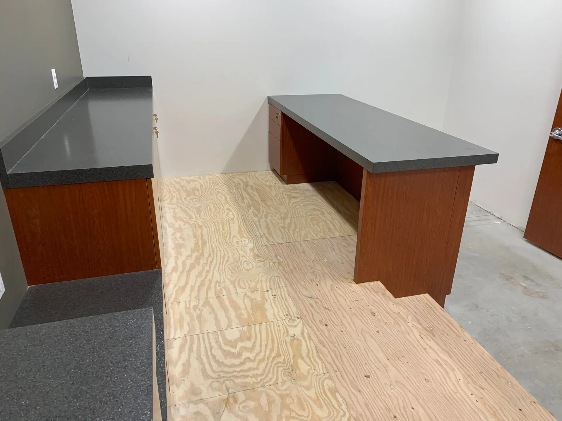 Sparse room with two gray-topped wooden desks on a plywood floor