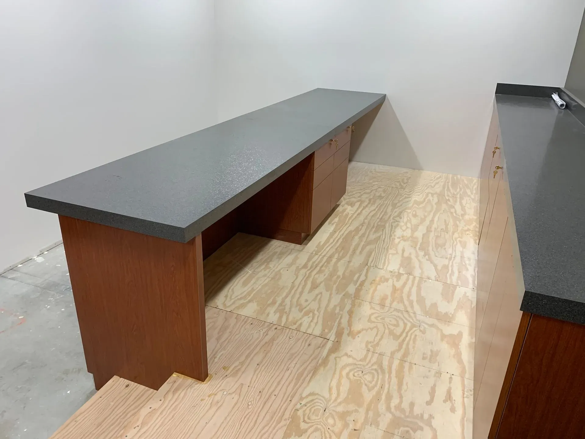 Long black countertop desk with wooden base in an empty room, near a wall and concrete floor