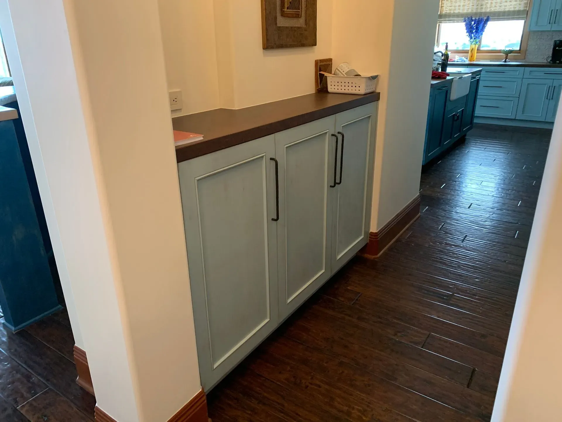 Kitchen hallway with pale blue cabinets, dark countertop, and wood floors