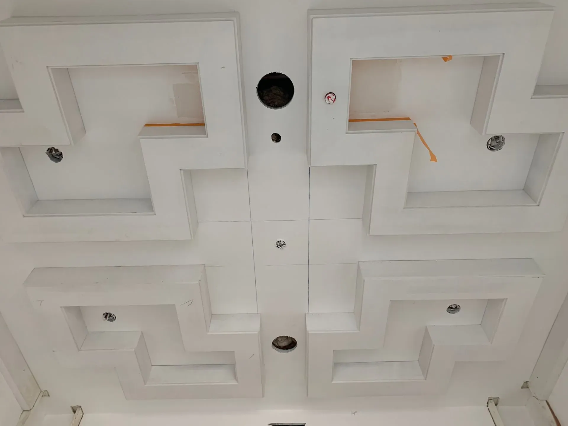 Ceiling with four white recessed geometric panels and small light fixtures, viewed from below