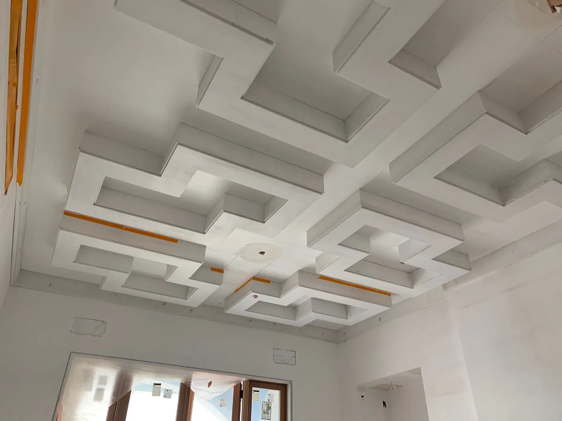 White room ceiling with geometric recessed panels and orange accent strips, seen from below