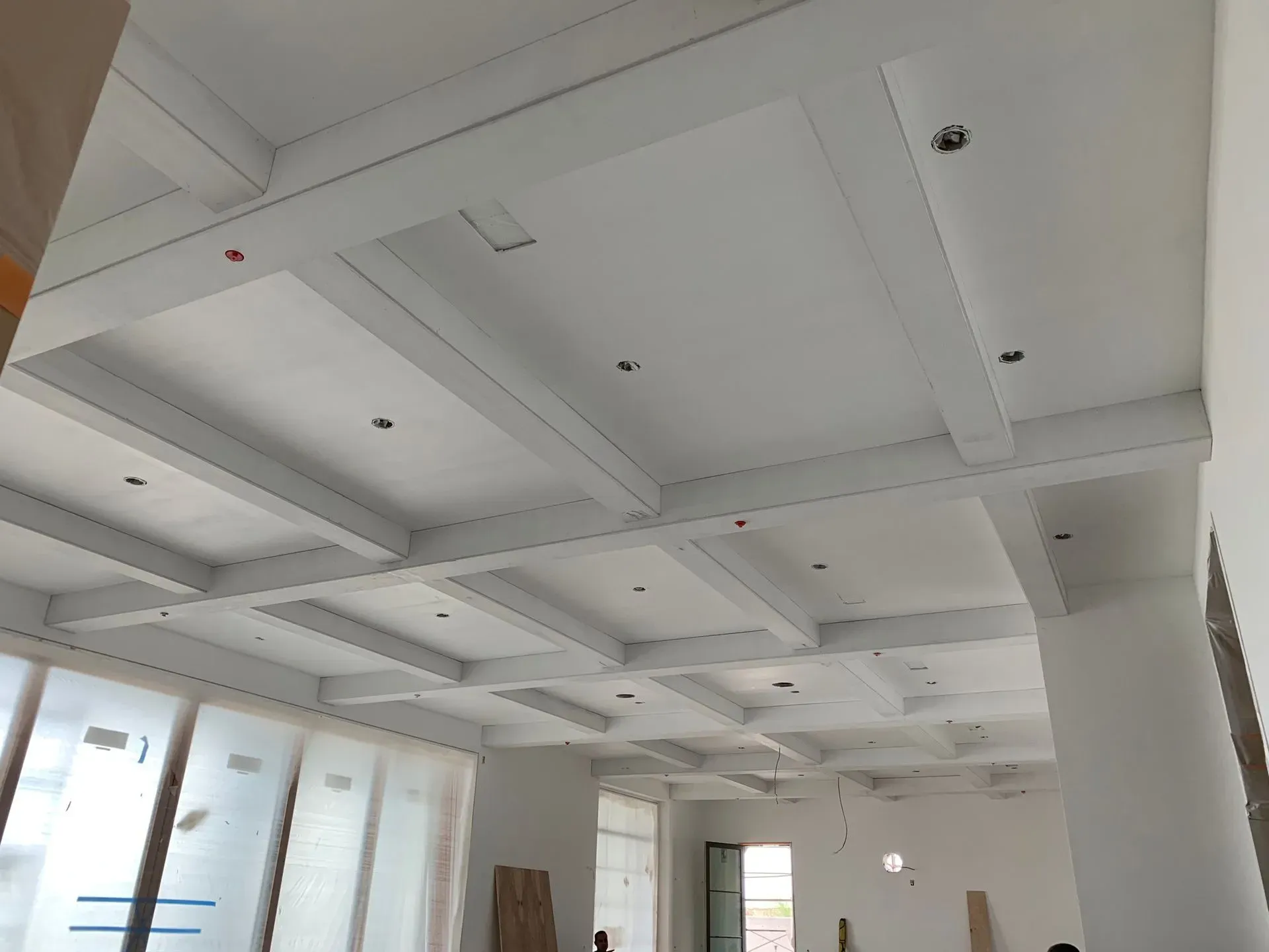 White coffered ceiling with recessed lights in a bright, unfinished room