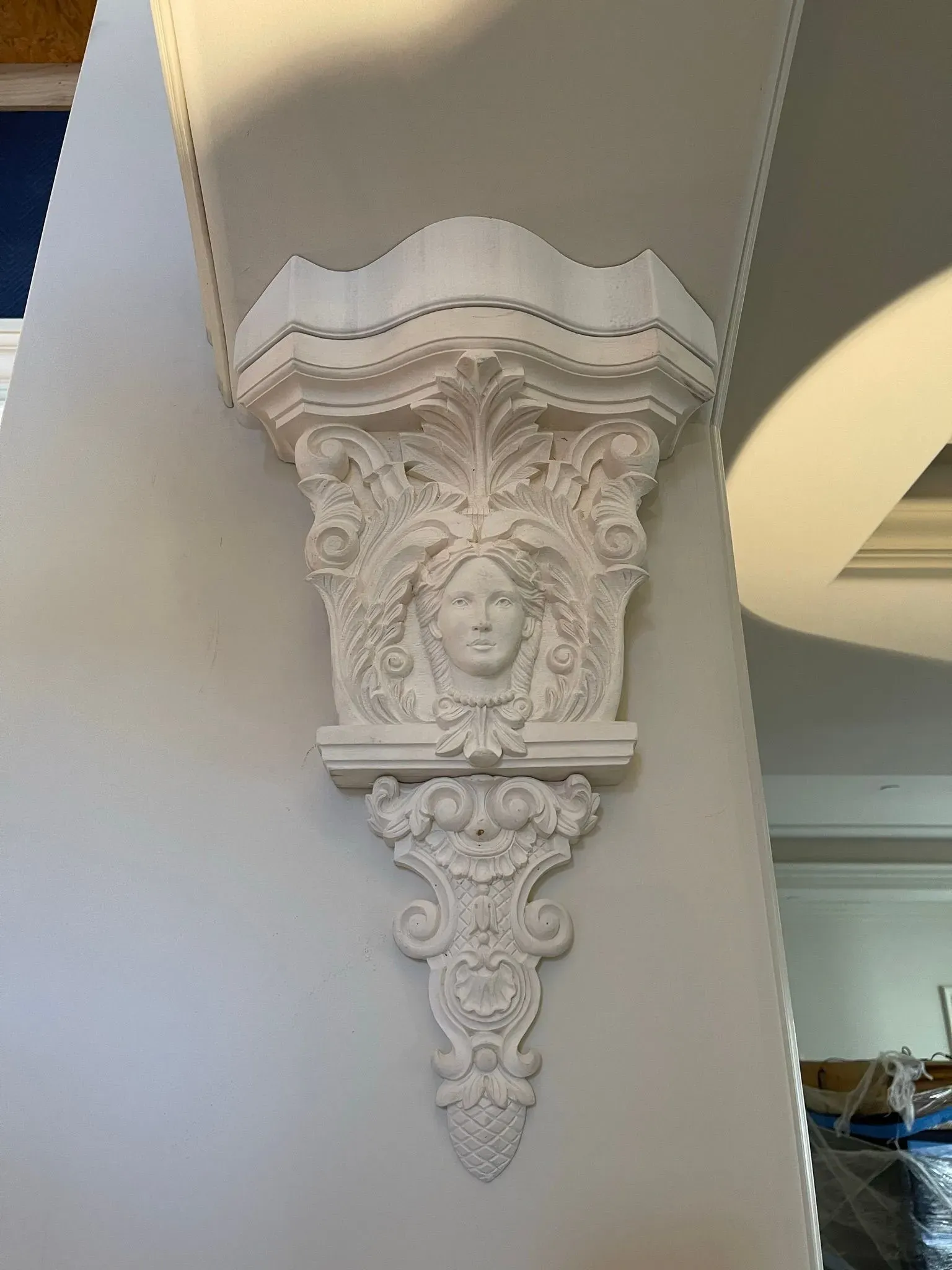 Ornate white plaster corbel with floral carving under a ceiling beam in an interior room