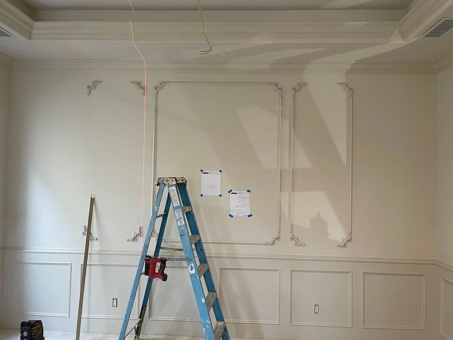 Blue ladder in a partially painted room with wall trim and paint test patches on the wall
