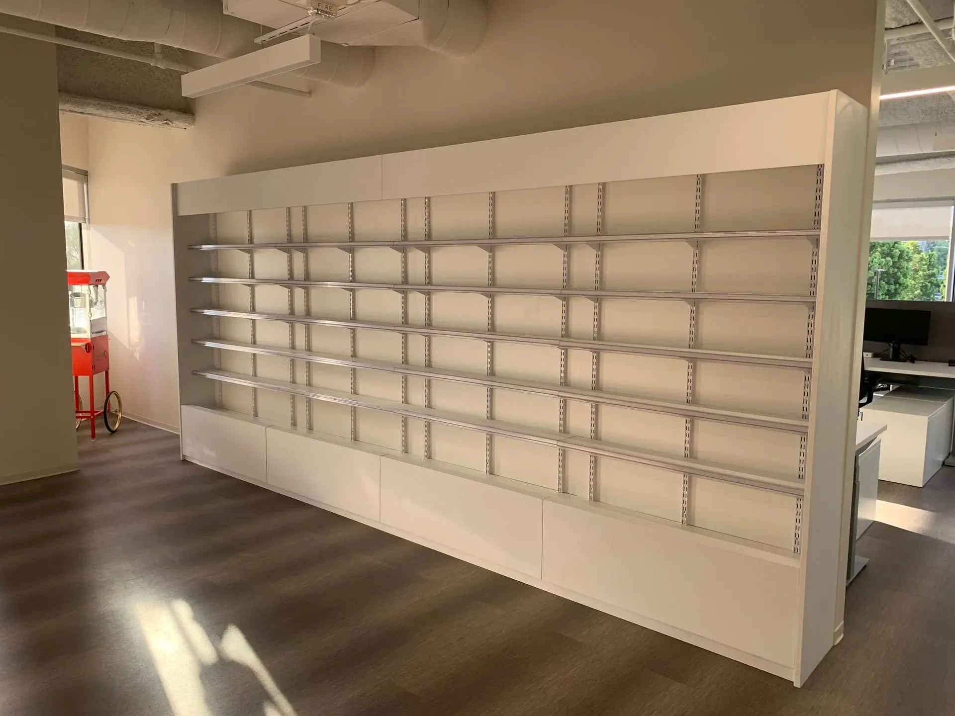 Empty white shelving wall in a bright modern interior space, with sunlight casting floor shadows.