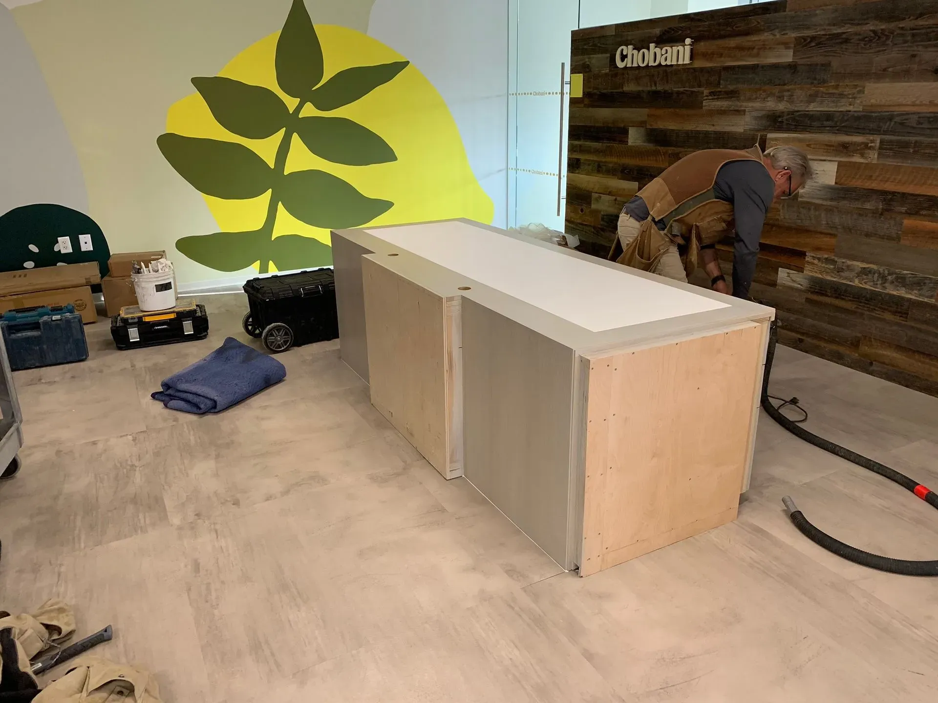Unfinished room with a wood cabinet, mural wall, and a worker installing wood paneling.