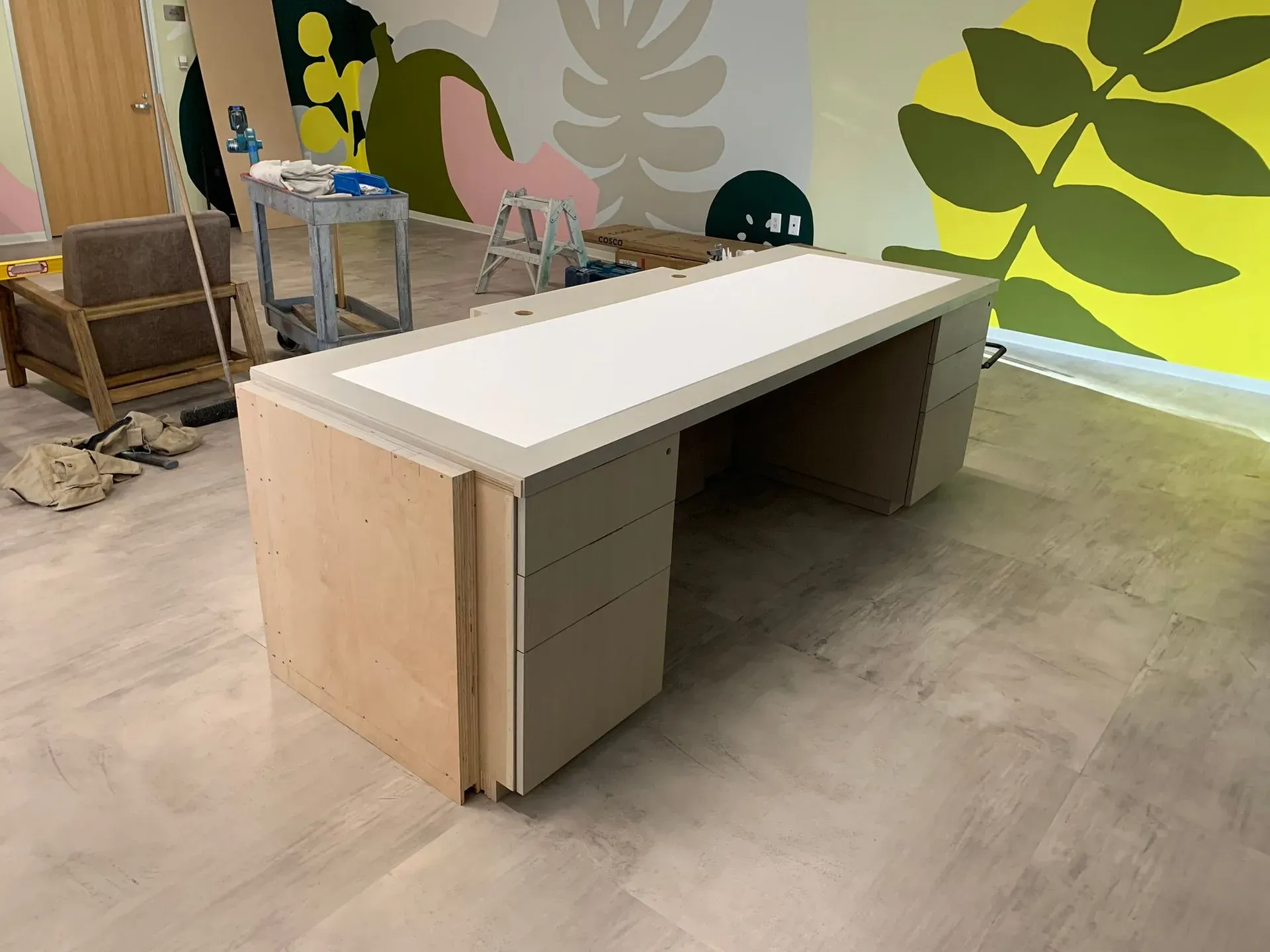 Modern office desk under construction with light wood sides and a white top in a colorful room